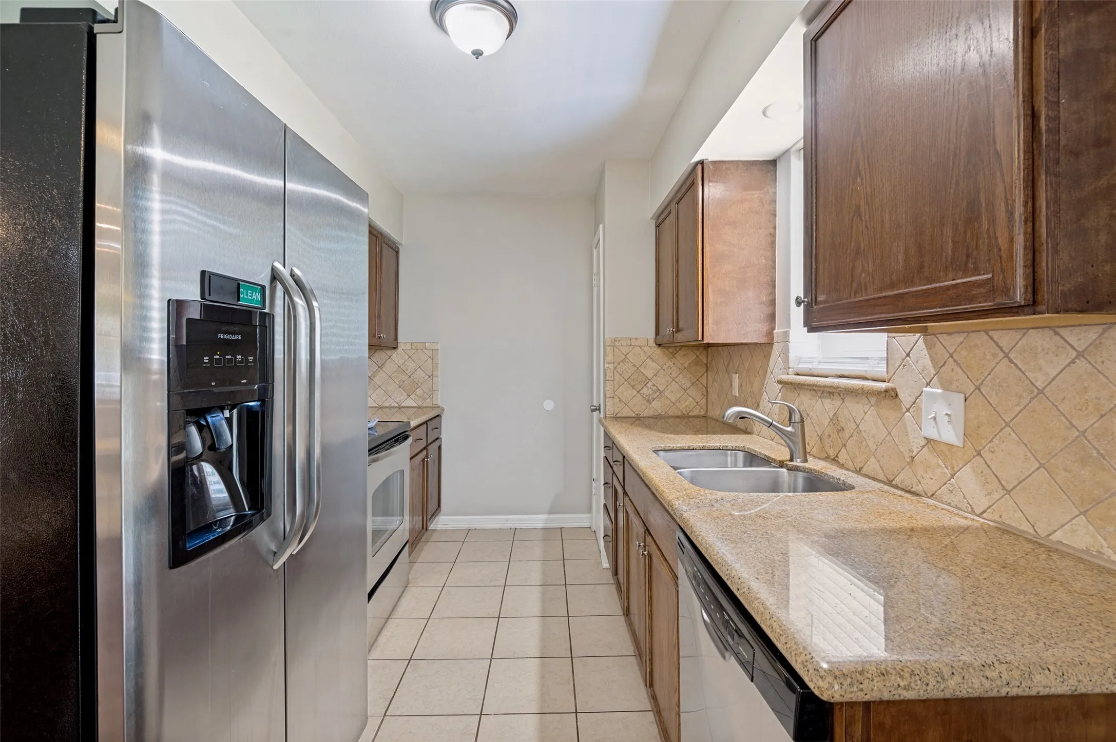 Kitchen featuring stainless steel appliances, wood cabinetry, granite-finish countertops, ceramic tile flooring and a tiled backsplash