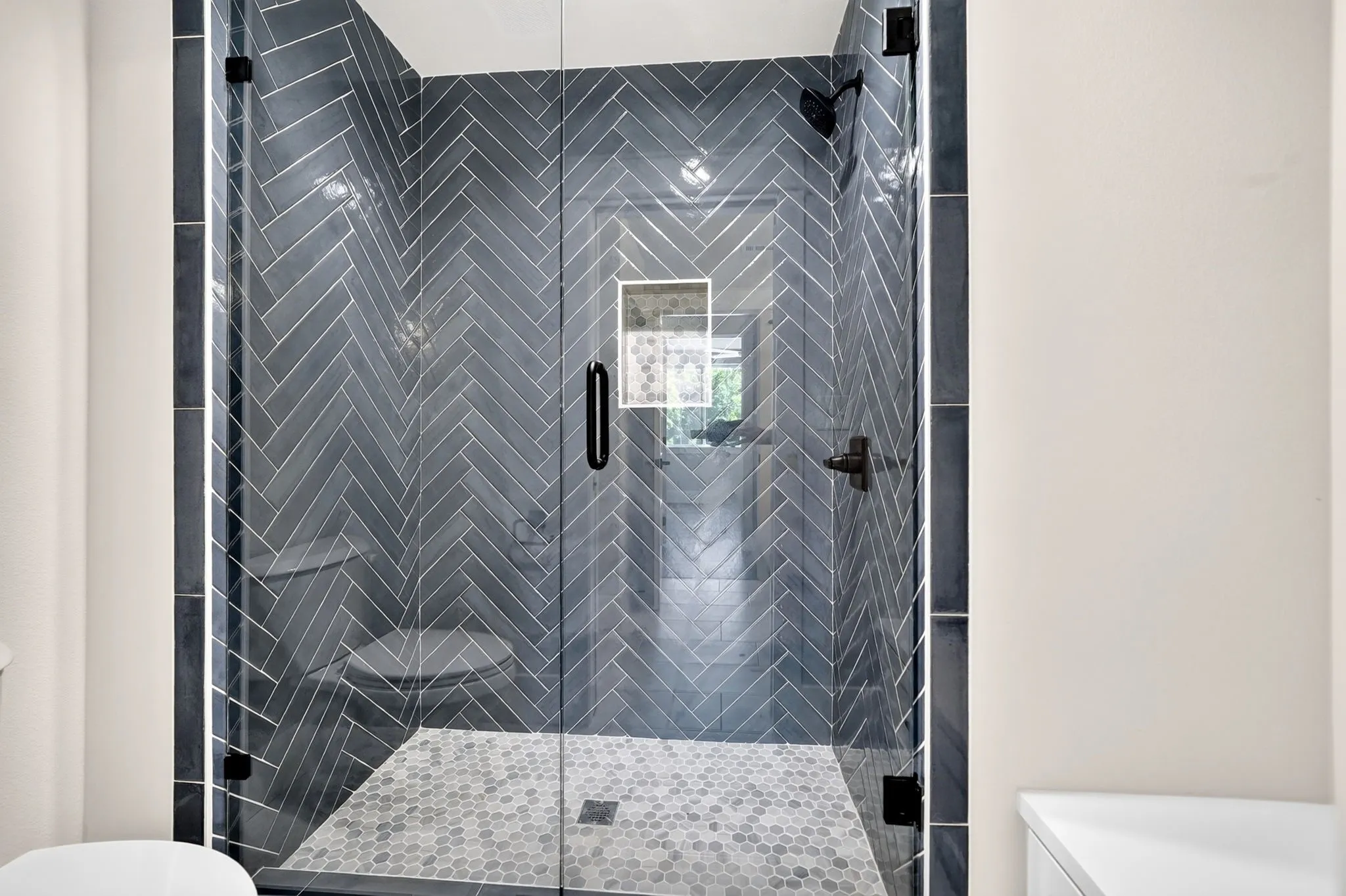 Spa-inspired walk-in shower with stylish herringbone tile, mosaic floor, and frameless glass door.