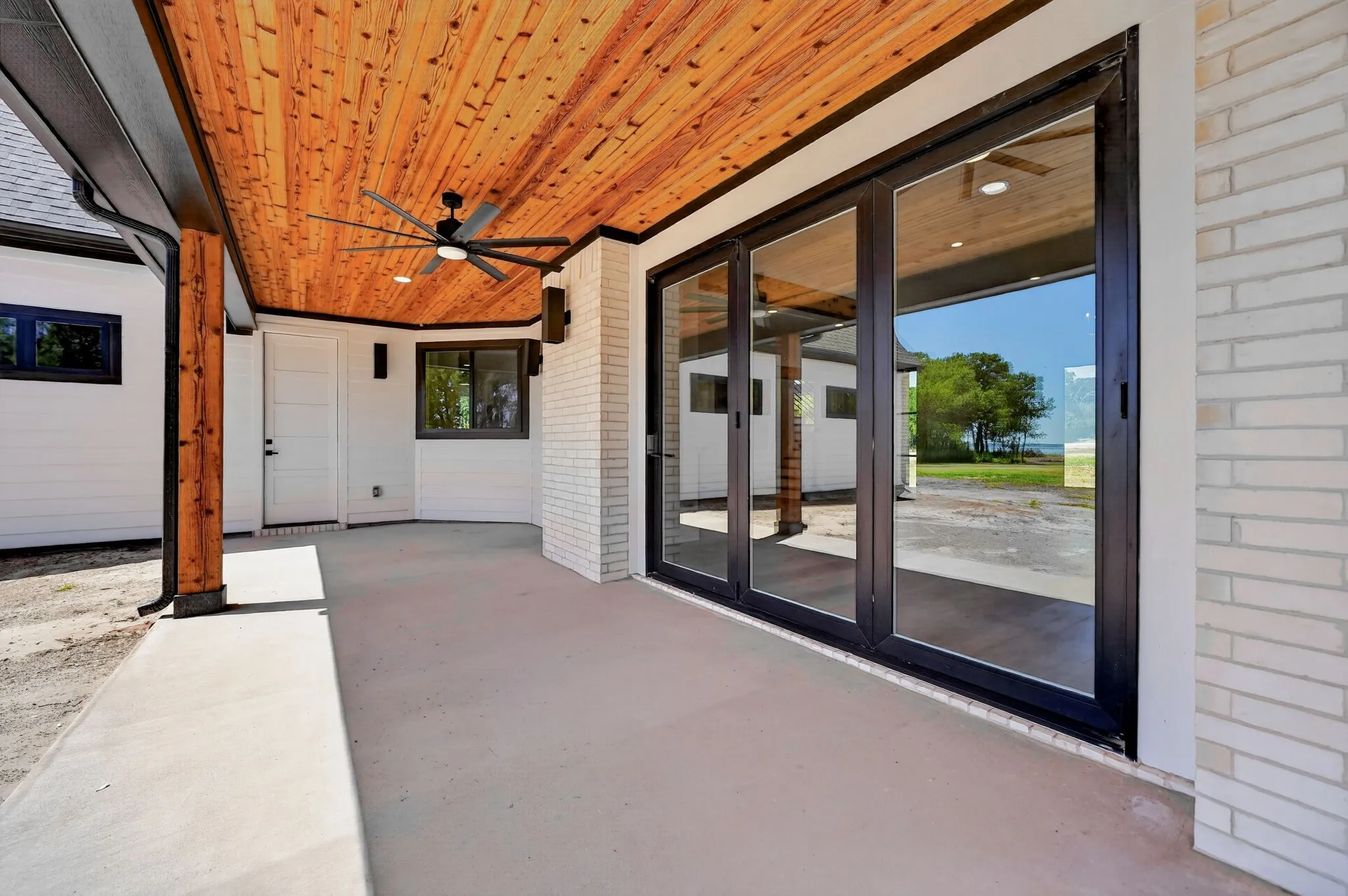Expansive back porch features a custom cedar ceiling with a sleek ceiling fan and robust wood accents.  The accordion door connects the exterior to the homes main living area.