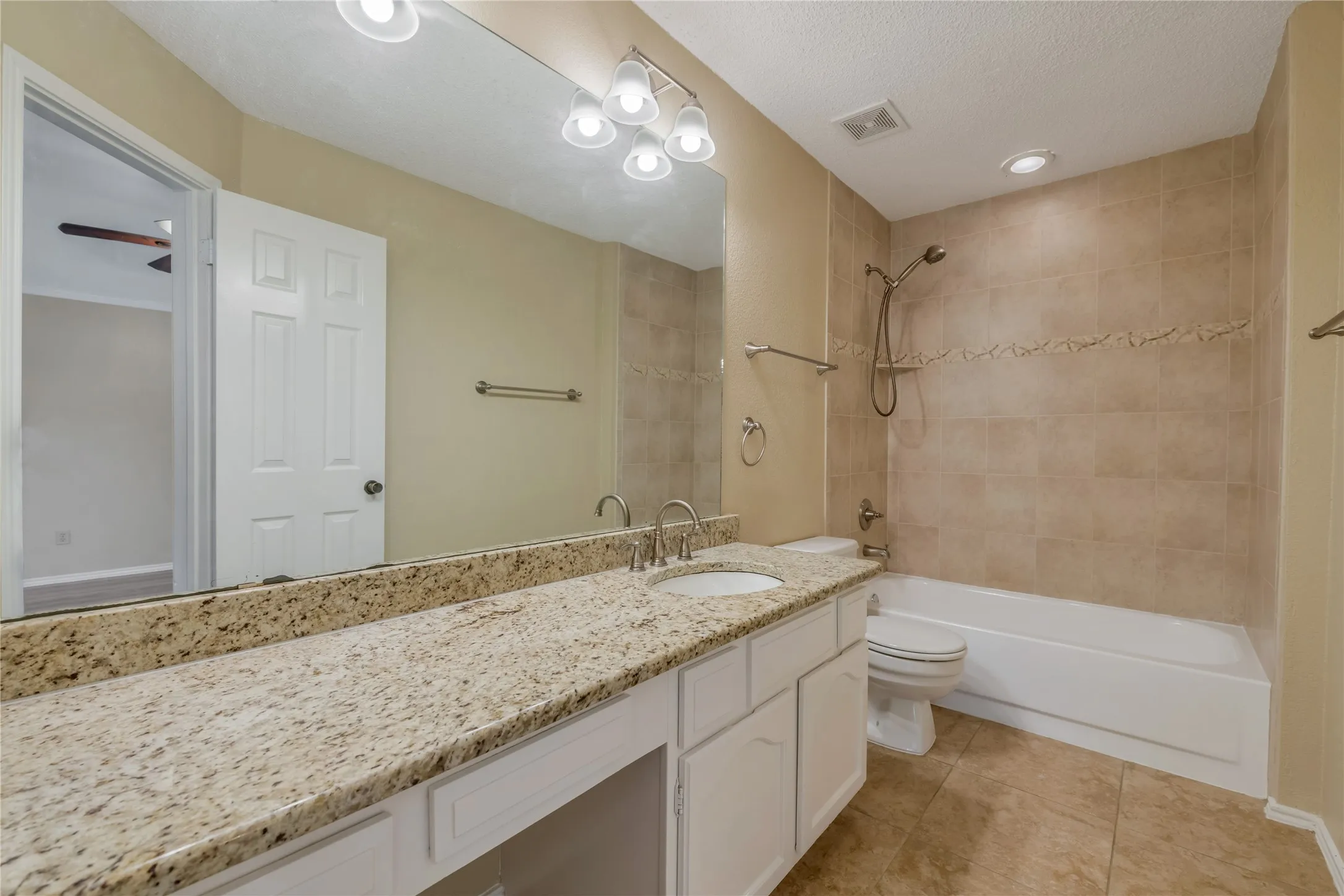Master Bathroom featuring a double vanity with stone countertops, a large mirror, and a combination tub/shower with tiled surround and decorative accent band