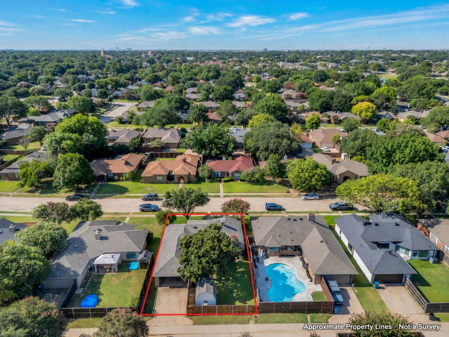 Expansive residential property featuring a gray shingled roof, a mature front yard tree, a paved driveway, and a backyard storage shed