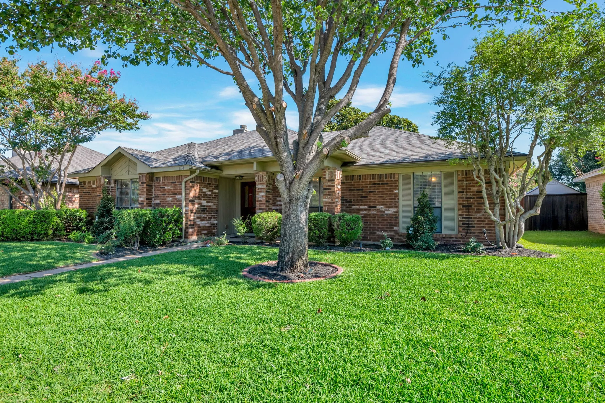 Brick exterior with a gabled roofline, mature trees, and landscaping
