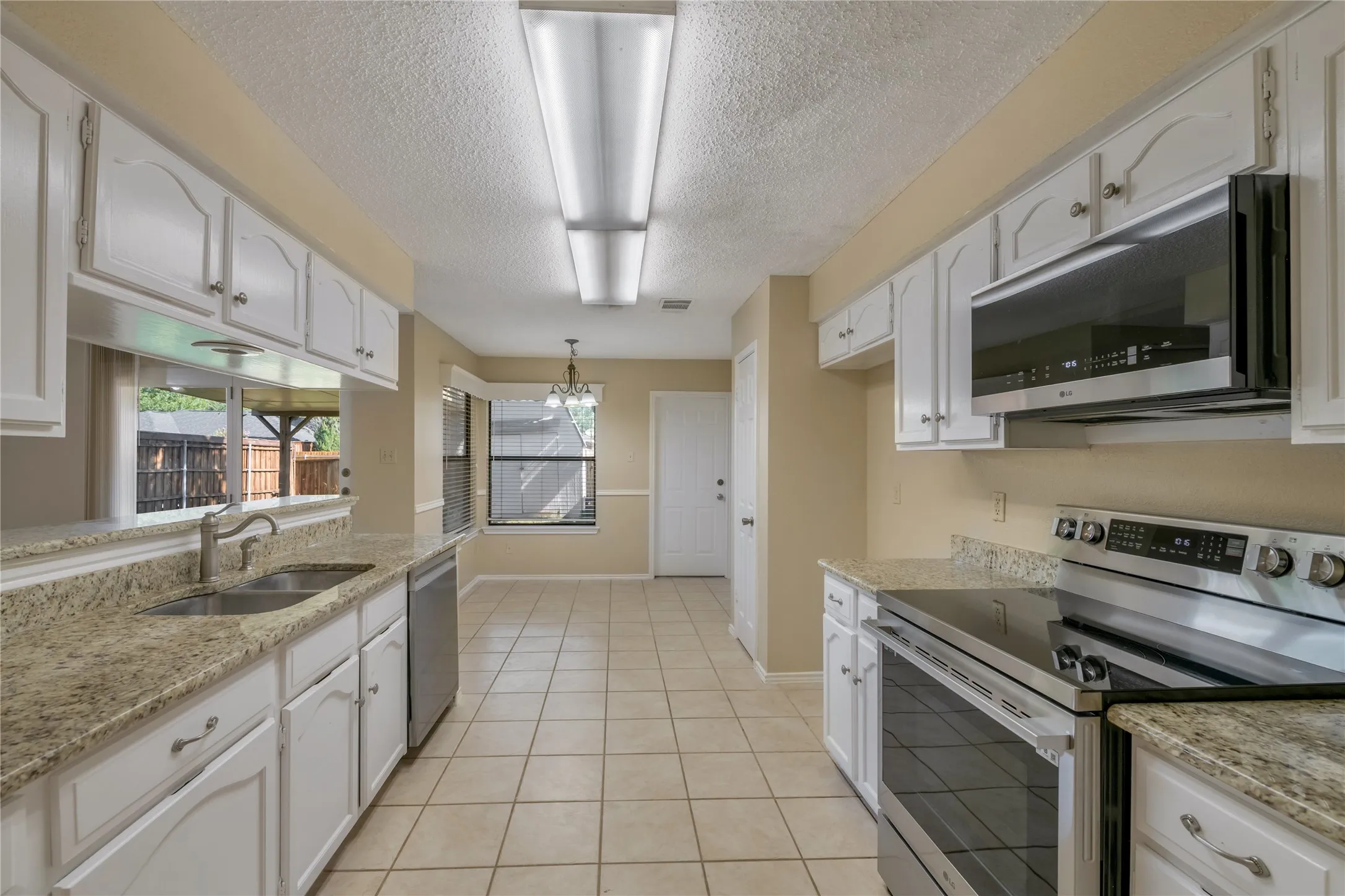 Kitchen featuring white cabinetry, granite countertops, stainless steel appliances, tile flooring, and a pass-through window
