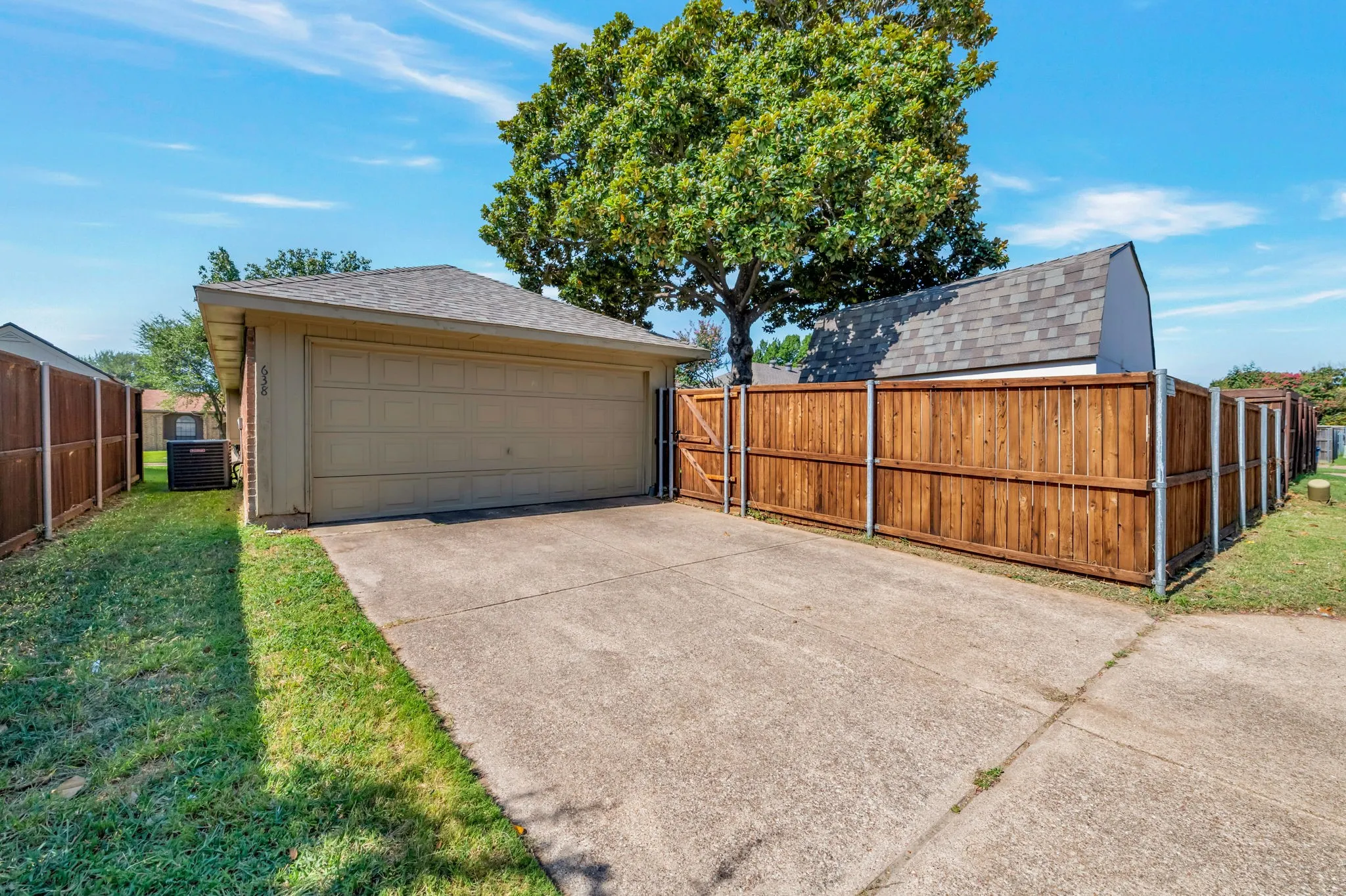 Concrete driveway with an attached garage, wood fence with gate, and manicured lawn