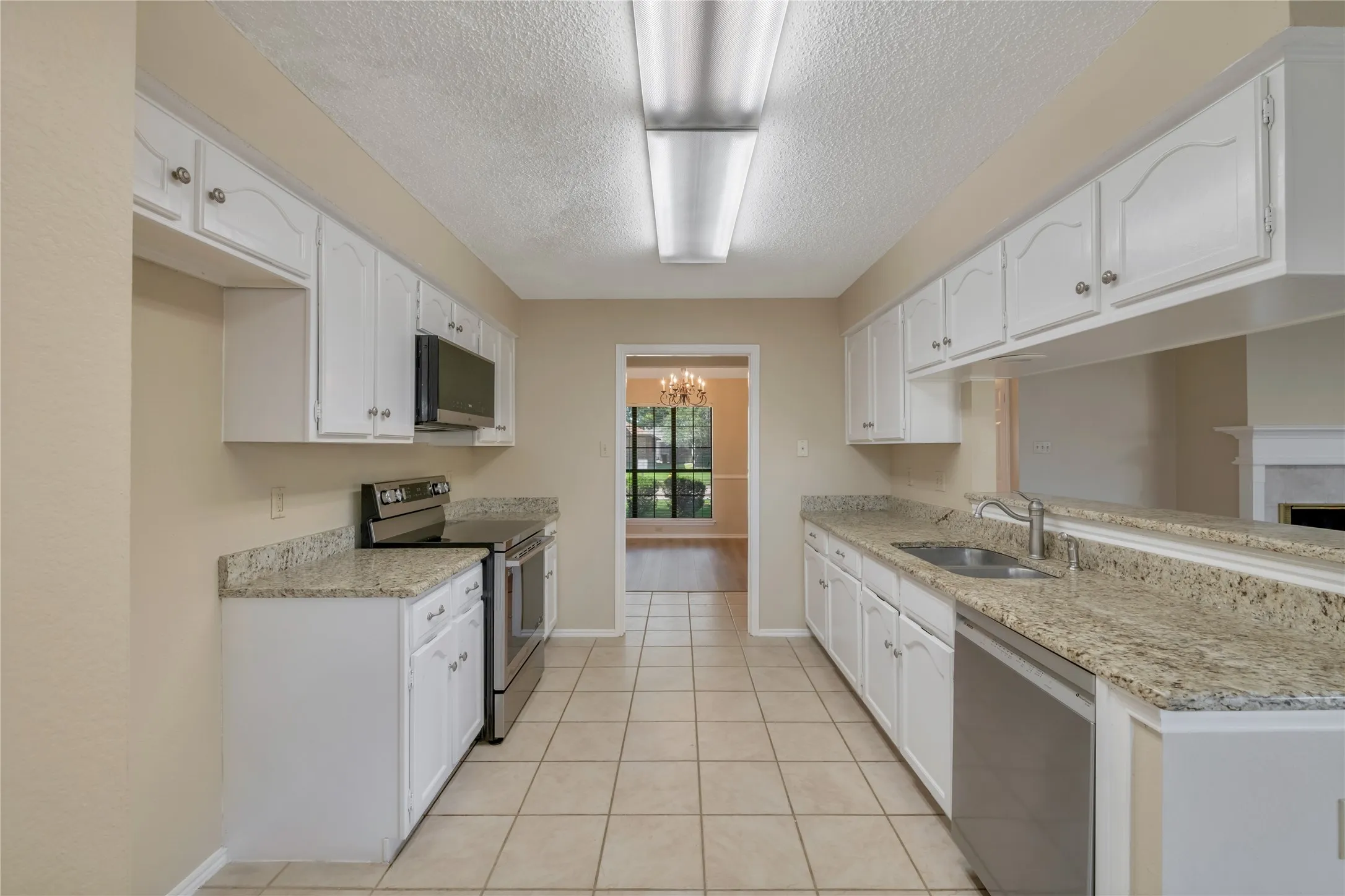 Kitchen featuring white cabinetry, light-toned granite countertops, stainless steel appliances, and ceramic tile flooring