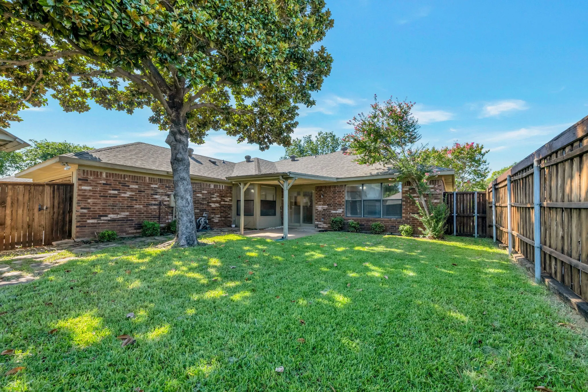 Expansive backyard featuring a manicured lawn, established trees, and a covered patio area