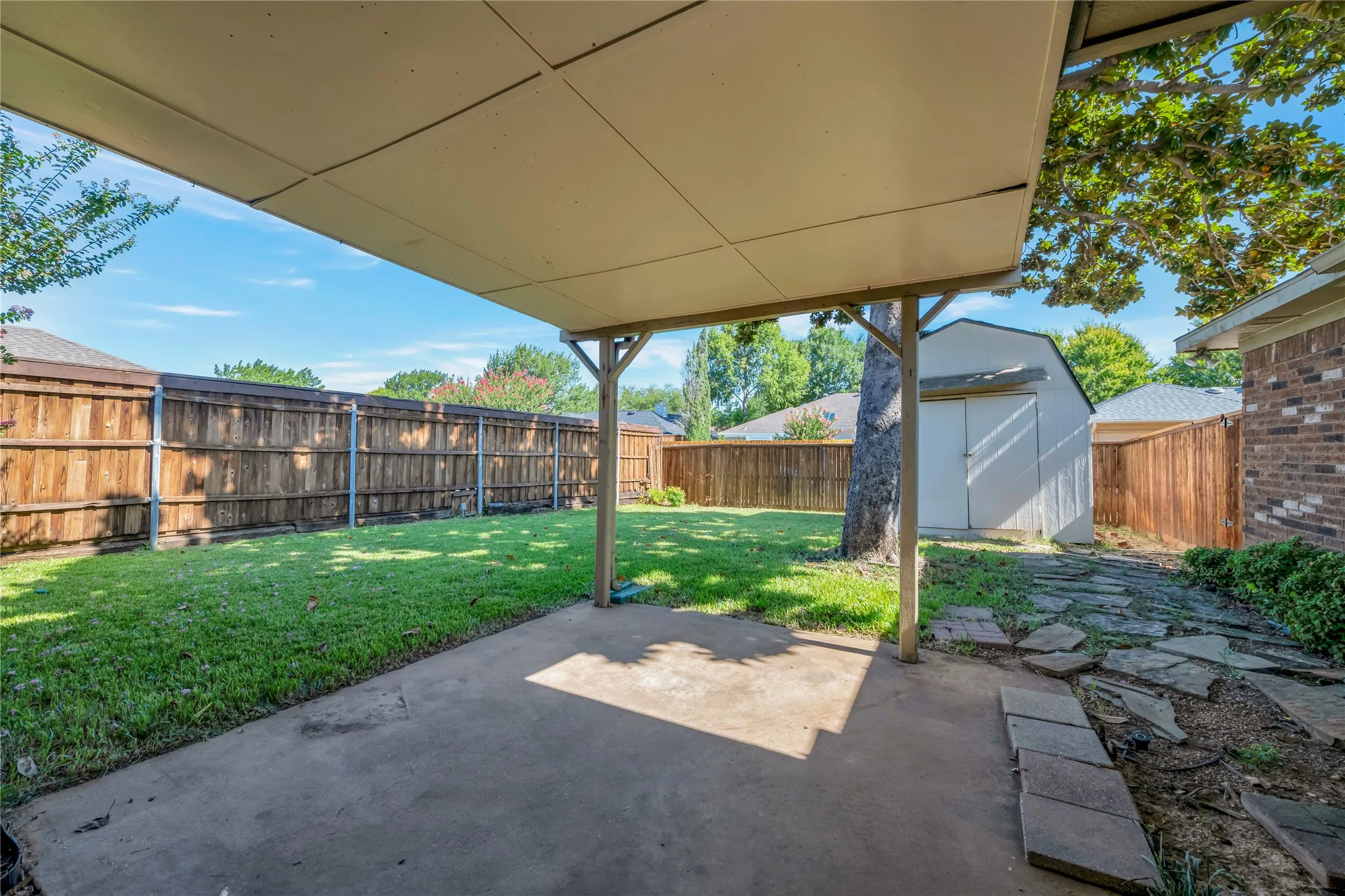 Covered patio with concrete flooring, overlooking a green lawn and privacy fencing