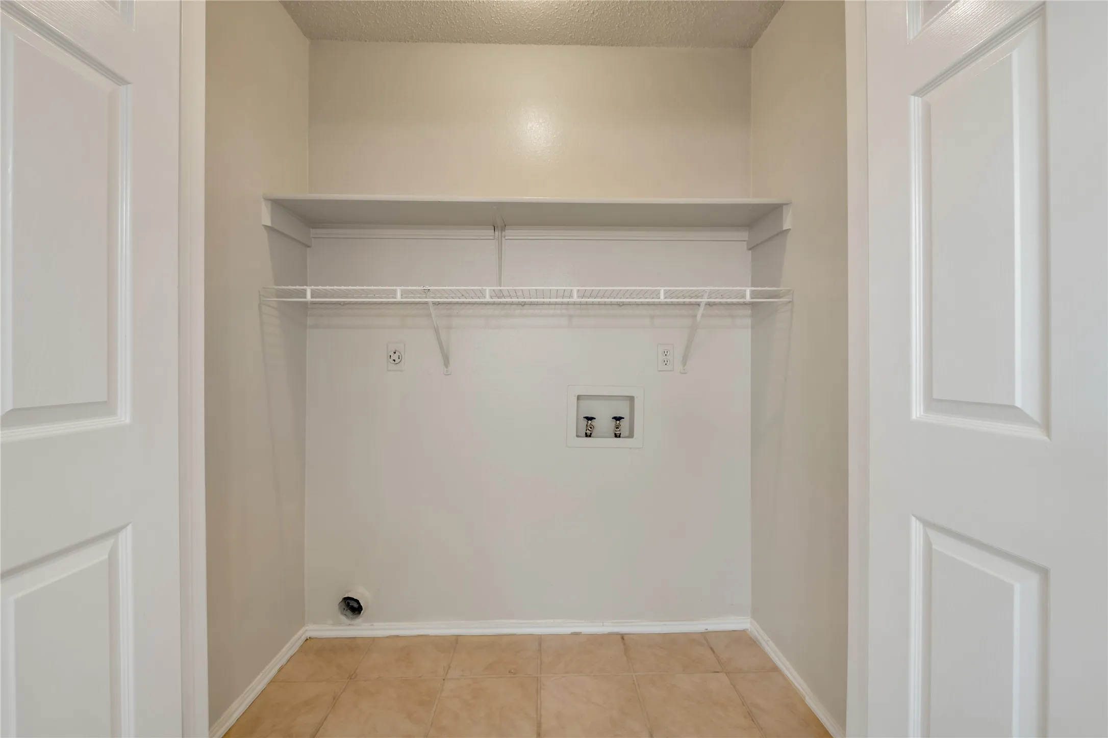 Dedicated utility space featuring tile flooring, wire shelving, and overhead storage