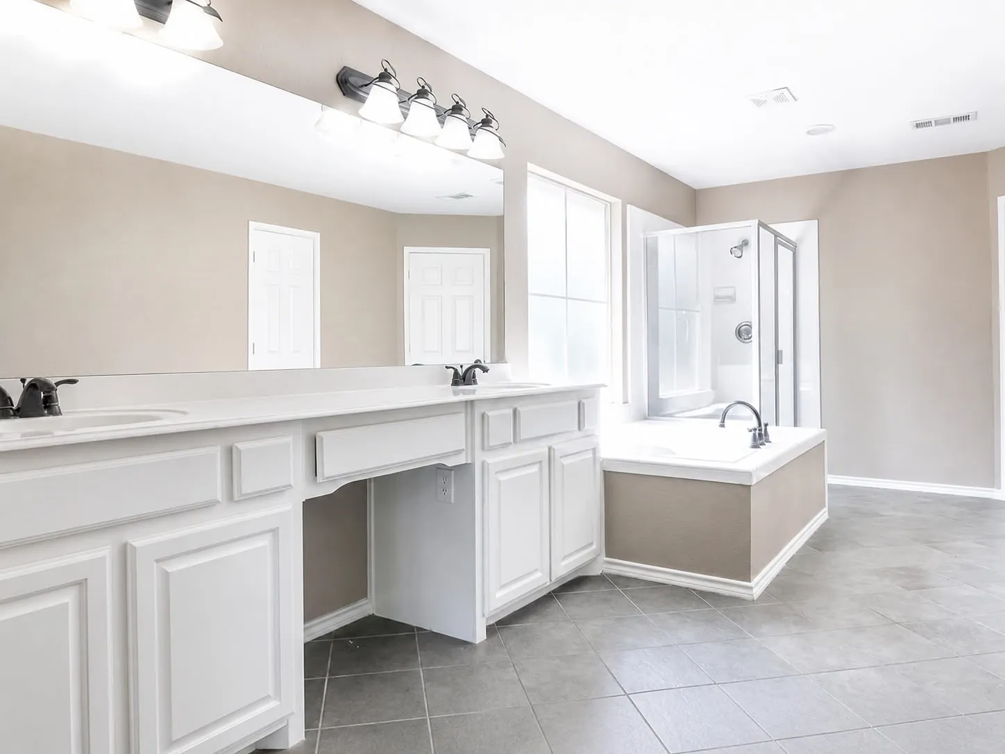 Spacious bathroom featuring a double vanity with white cabinetry, a large built-in mirror, a separate shower enclosure, a soaking tub, and gray tile flooring