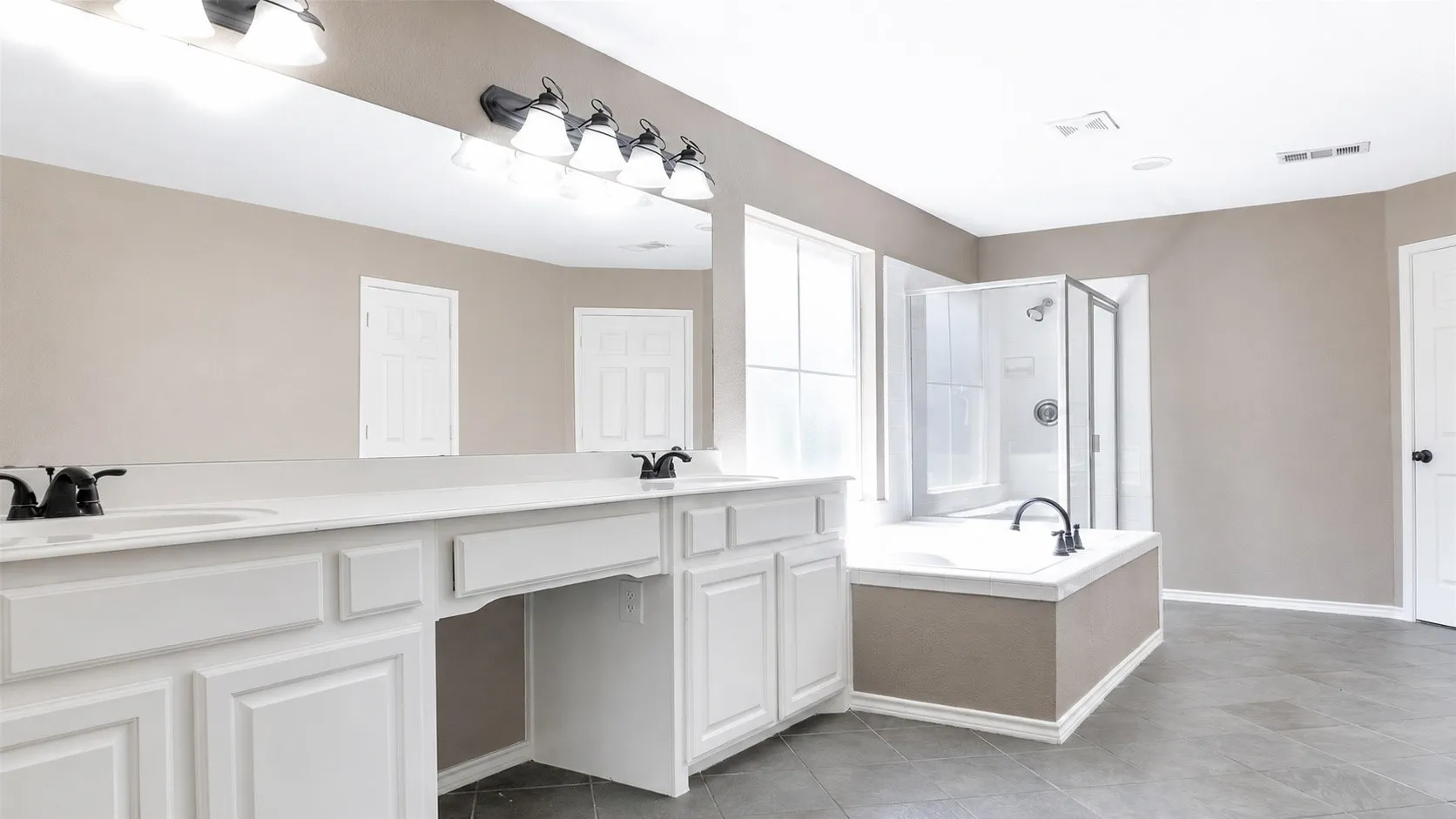 Spacious bathroom featuring a dual vanity with white cabinetry and a large mirror, a separate shower enclosure, a built-in soaking tub, and gray tile flooring