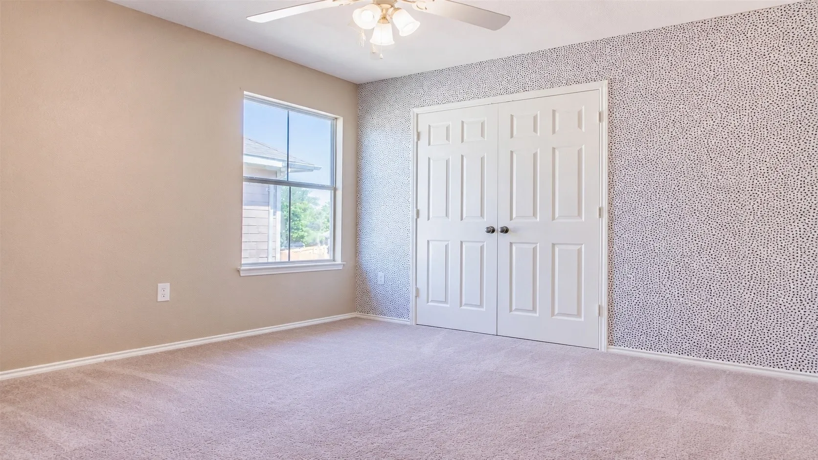 Carpeted room featuring a single window, a ceiling fan with light fixture, and double paneled doors