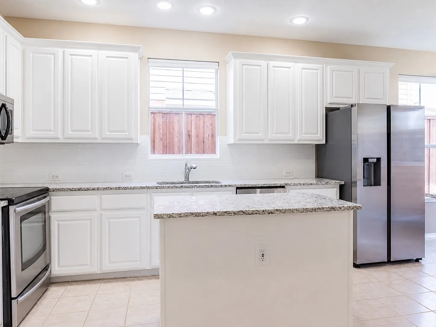 Modern kitchen featuring white shaker cabinetry, granite countertops, stainless steel appliances, a white subway tile backsplash, and recessed lighting