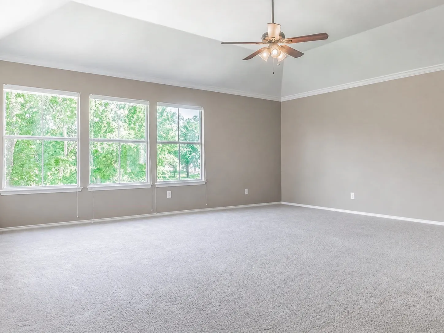 Spacious room featuring vaulted ceilings, crown molding, a ceiling fan, and three large windows