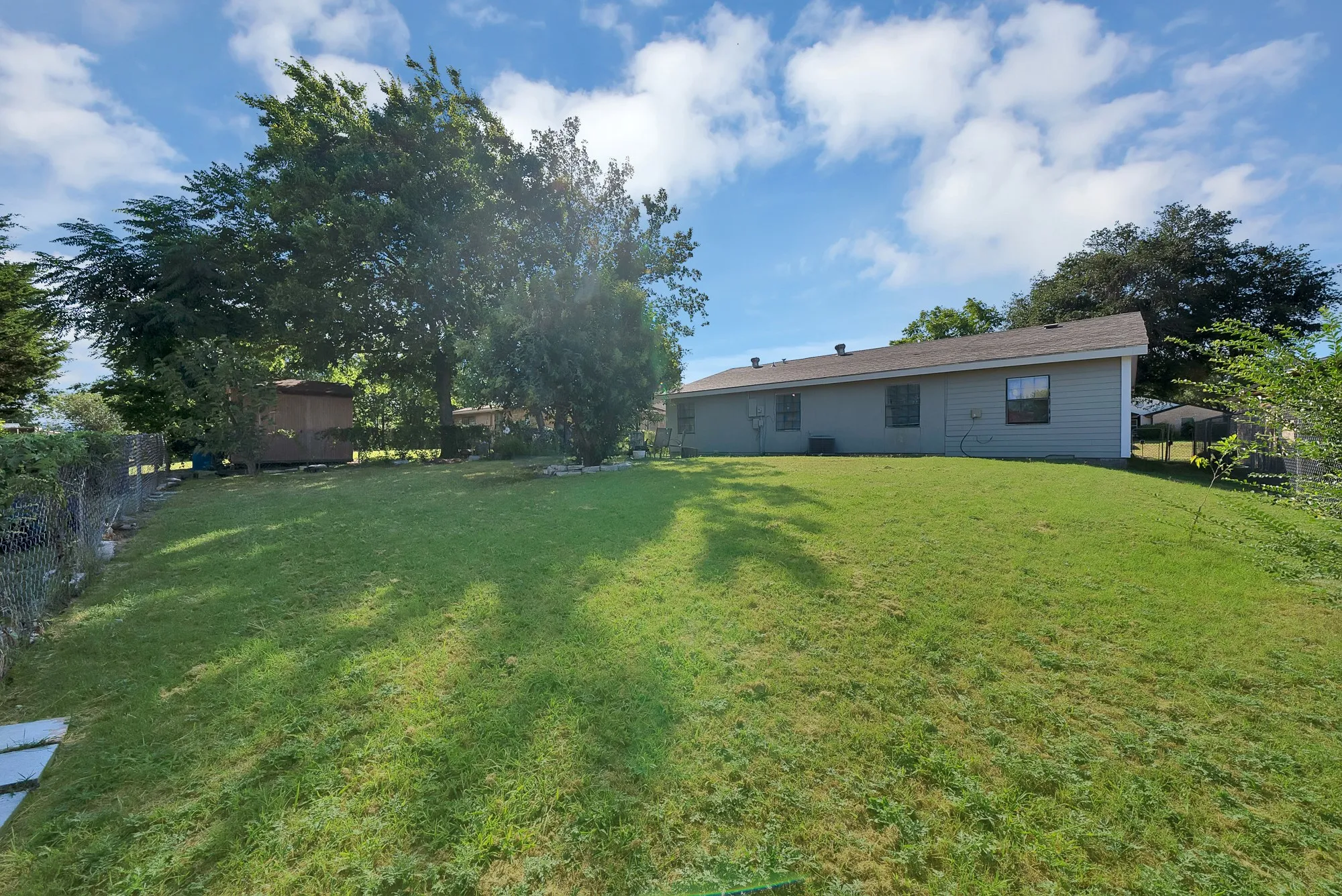 Expansive green lawn with mature trees and a detached shed, bordered by a chain-link fence