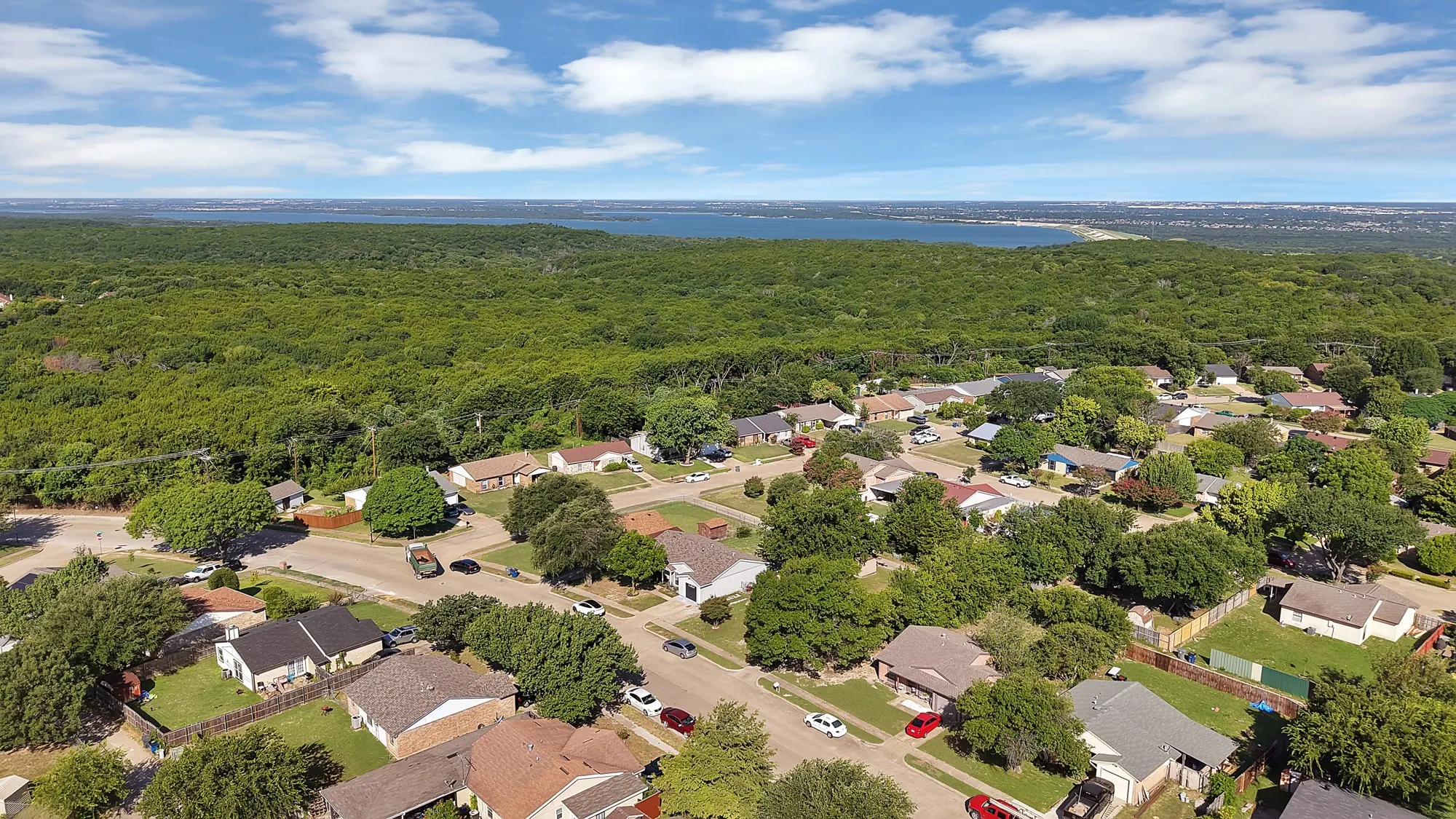 Aerial perspective showcasing a residential neighborhood bordering a substantial expanse of green space and a distant body of water
