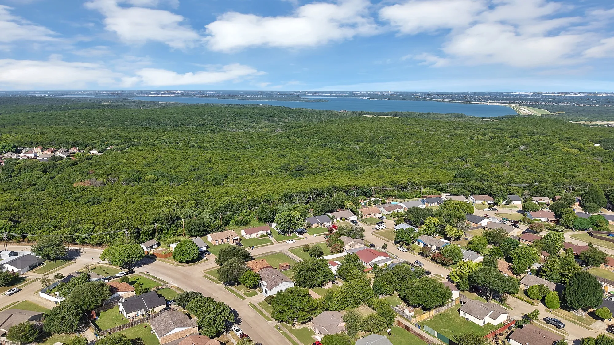 Aerial perspective showcasing a residential neighborhood bordering a large forested area and a substantial body of water