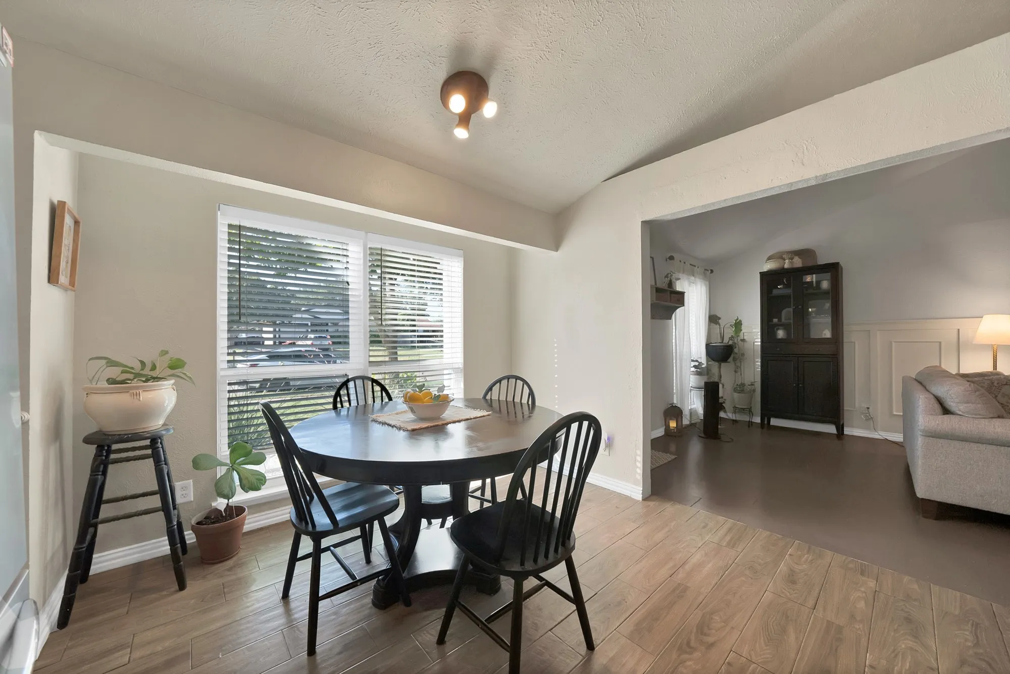 Dining area featuring wood-finish flooring, a large window with white blinds, and a multi-bulb ceiling light fixture