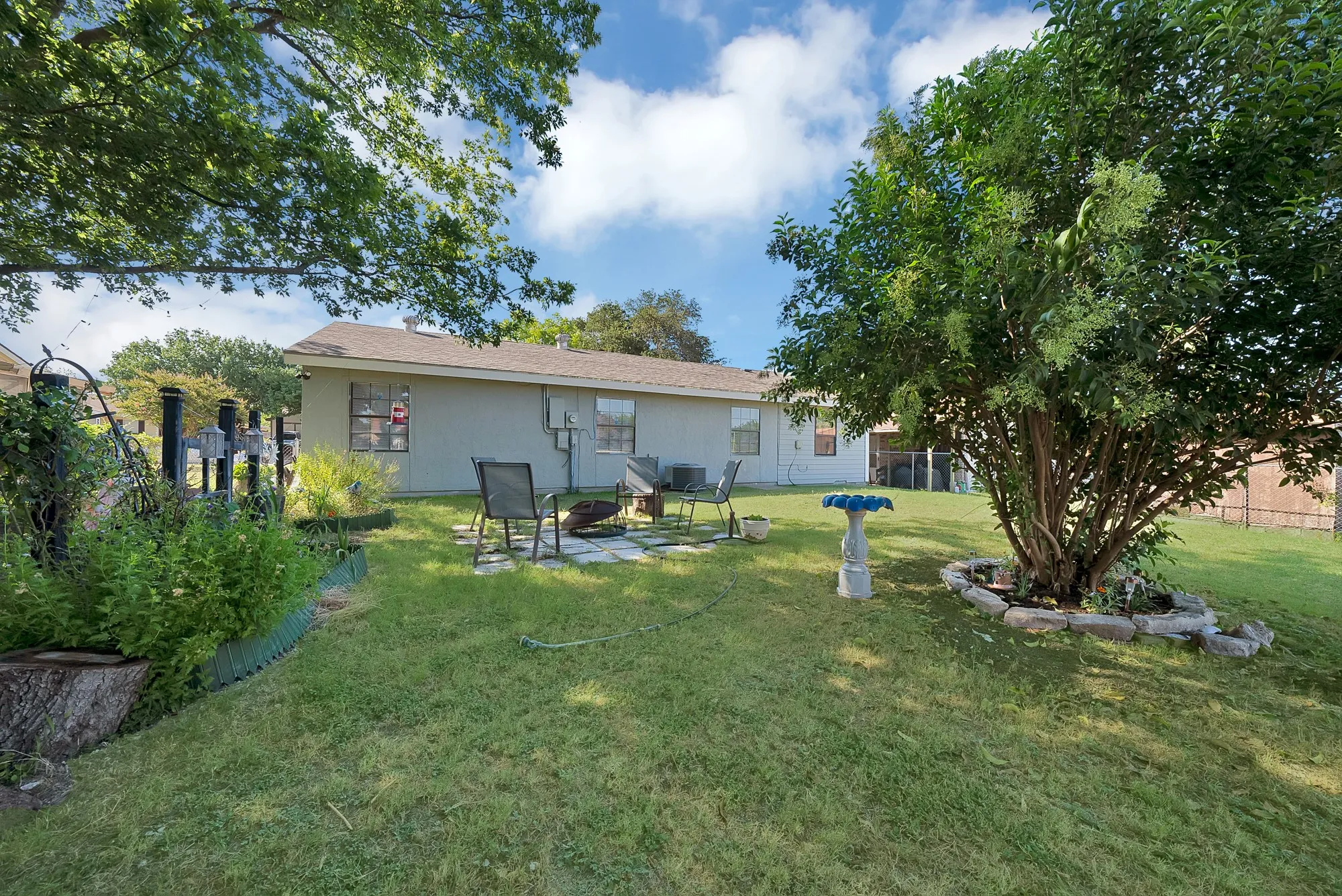 Spacious backyard featuring a manicured lawn, established trees, and a stone-paved patio area