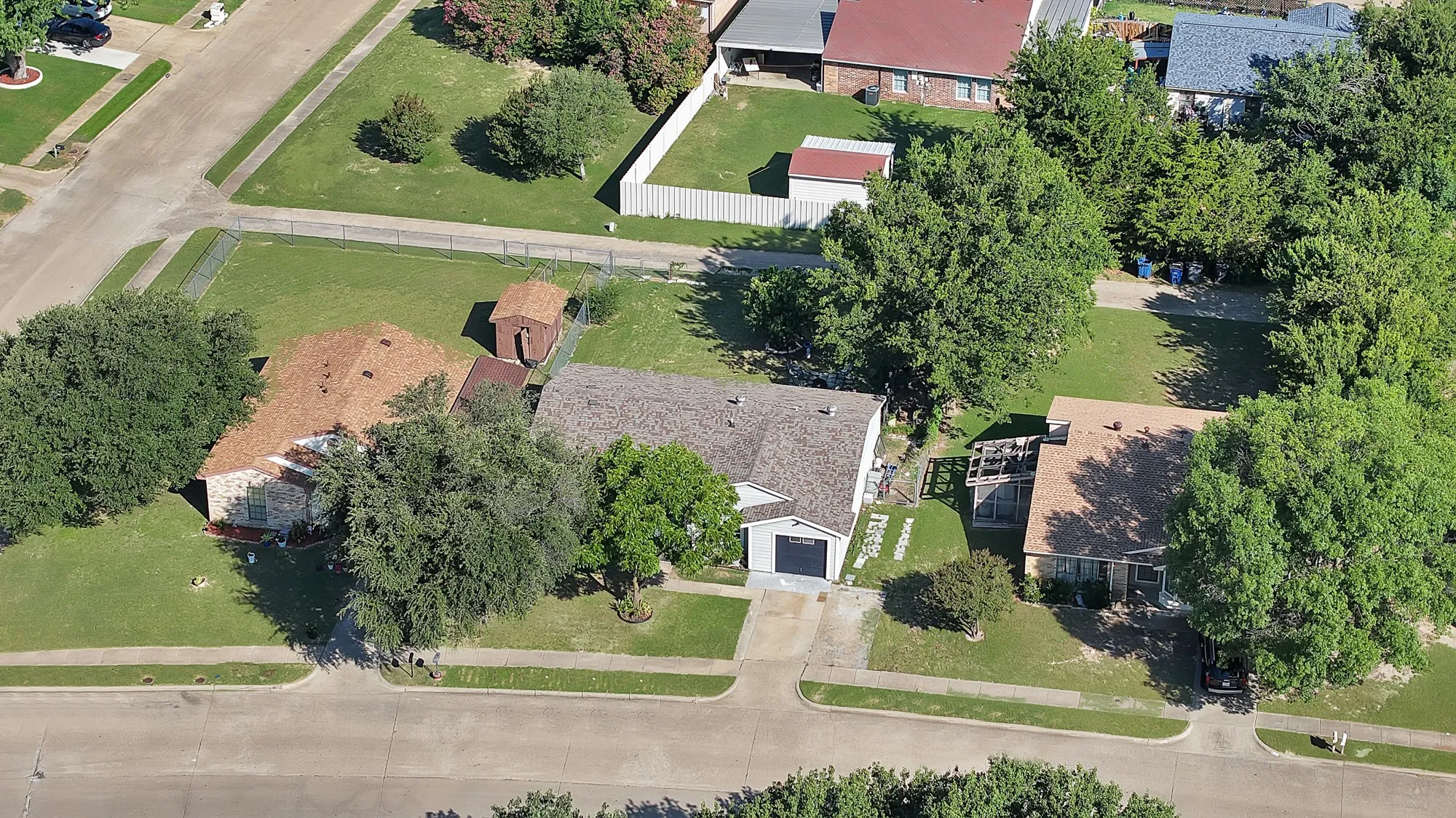 Aerial view of a residential property with a light-colored shingle roof, attached garage, and a concrete driveway