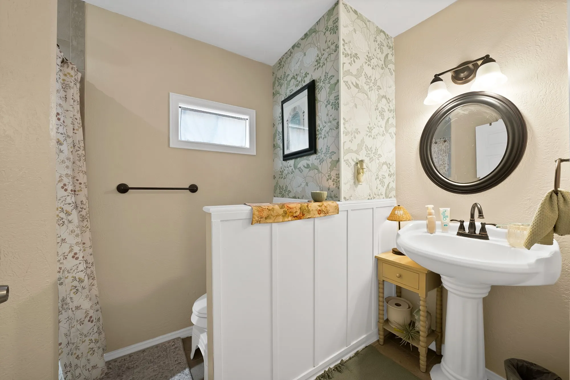 Bathroom featuring a pedestal sink, a circular framed mirror, and a two-light vanity fixture