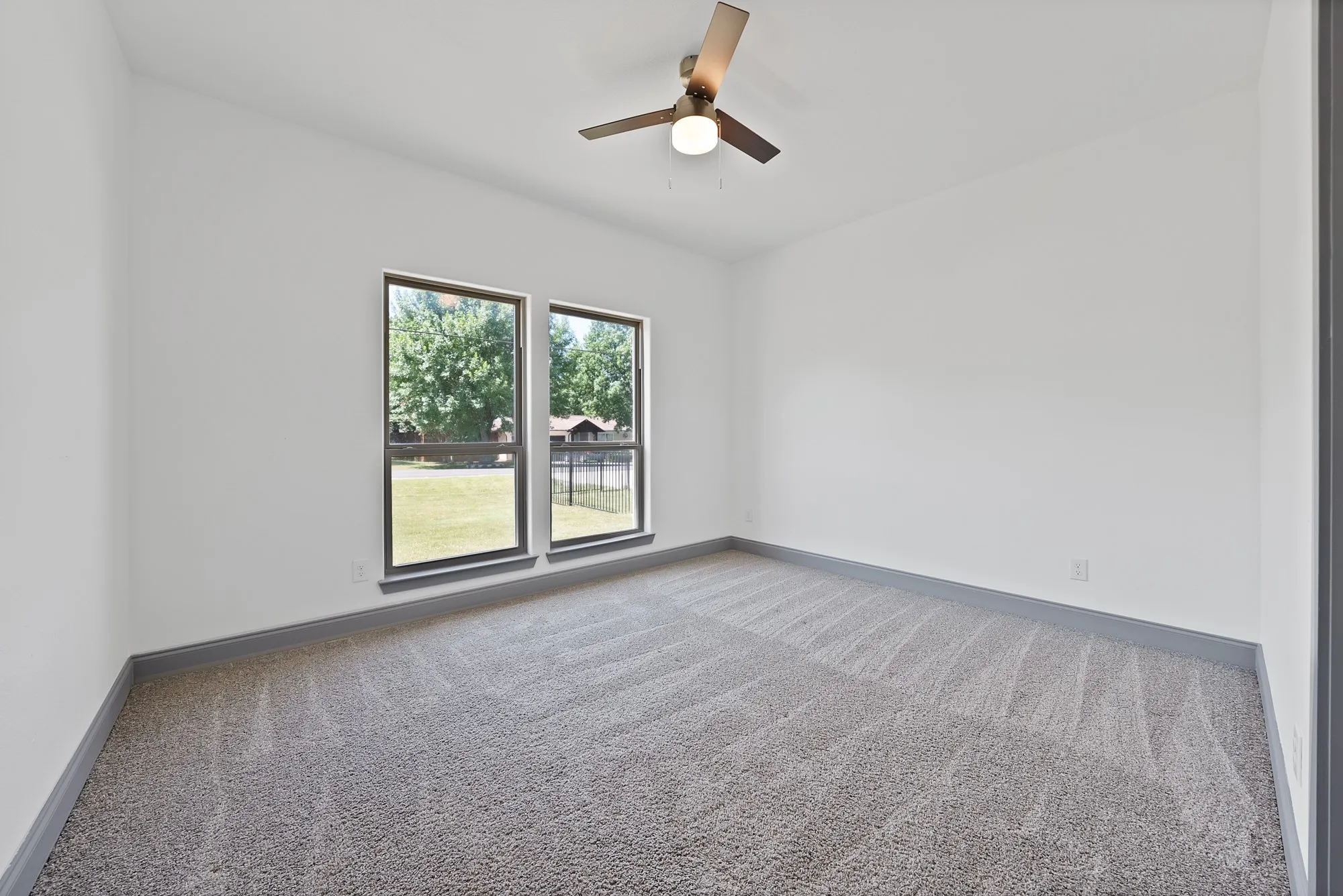 Carpeted room featuring two large windows with dark trim, white walls, and a ceiling fan with integrated lighting
