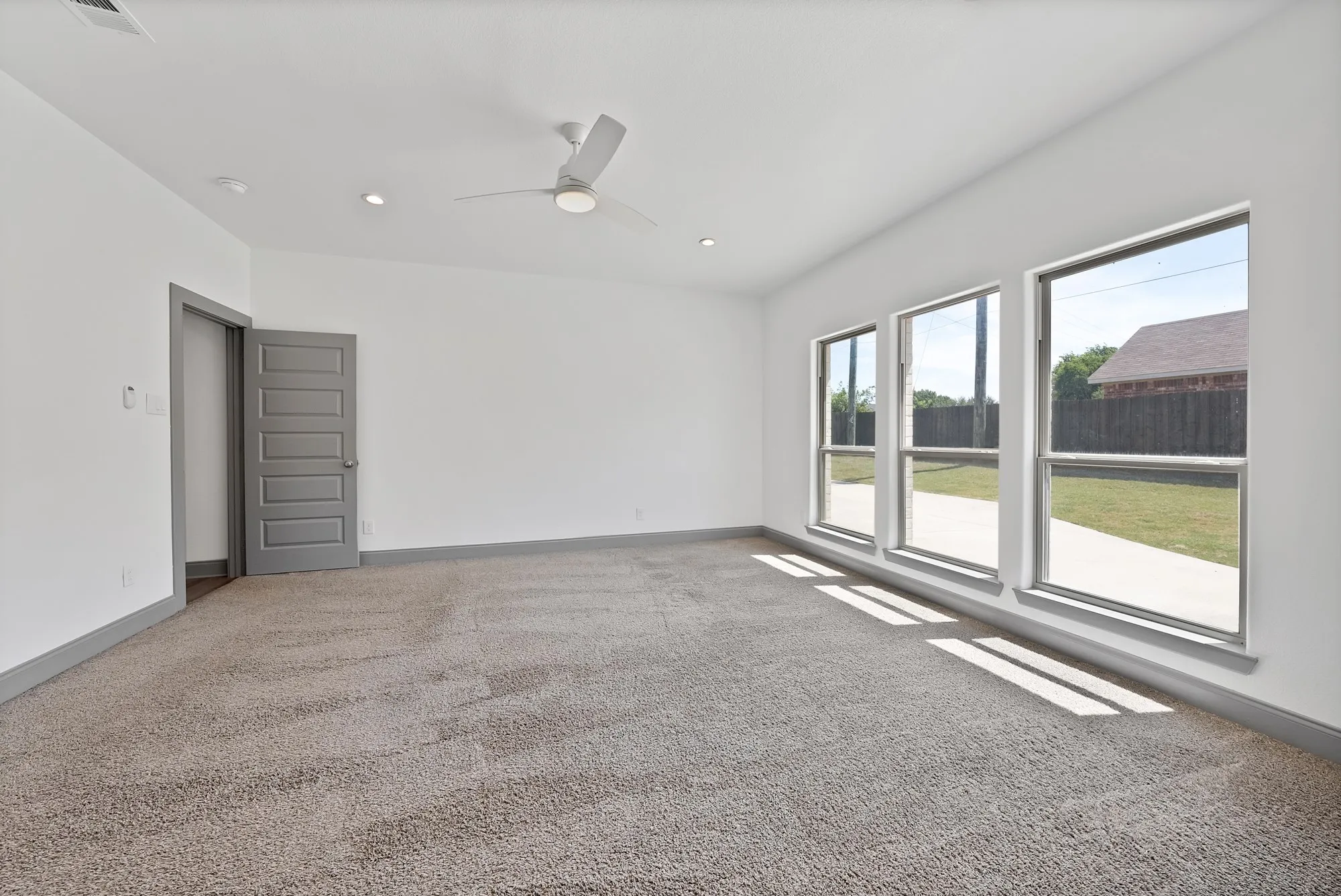 Spacious room featuring three large windows, plush carpet flooring, a modern ceiling fan, recessed lighting, and a five-panel interior door with matte gray trim