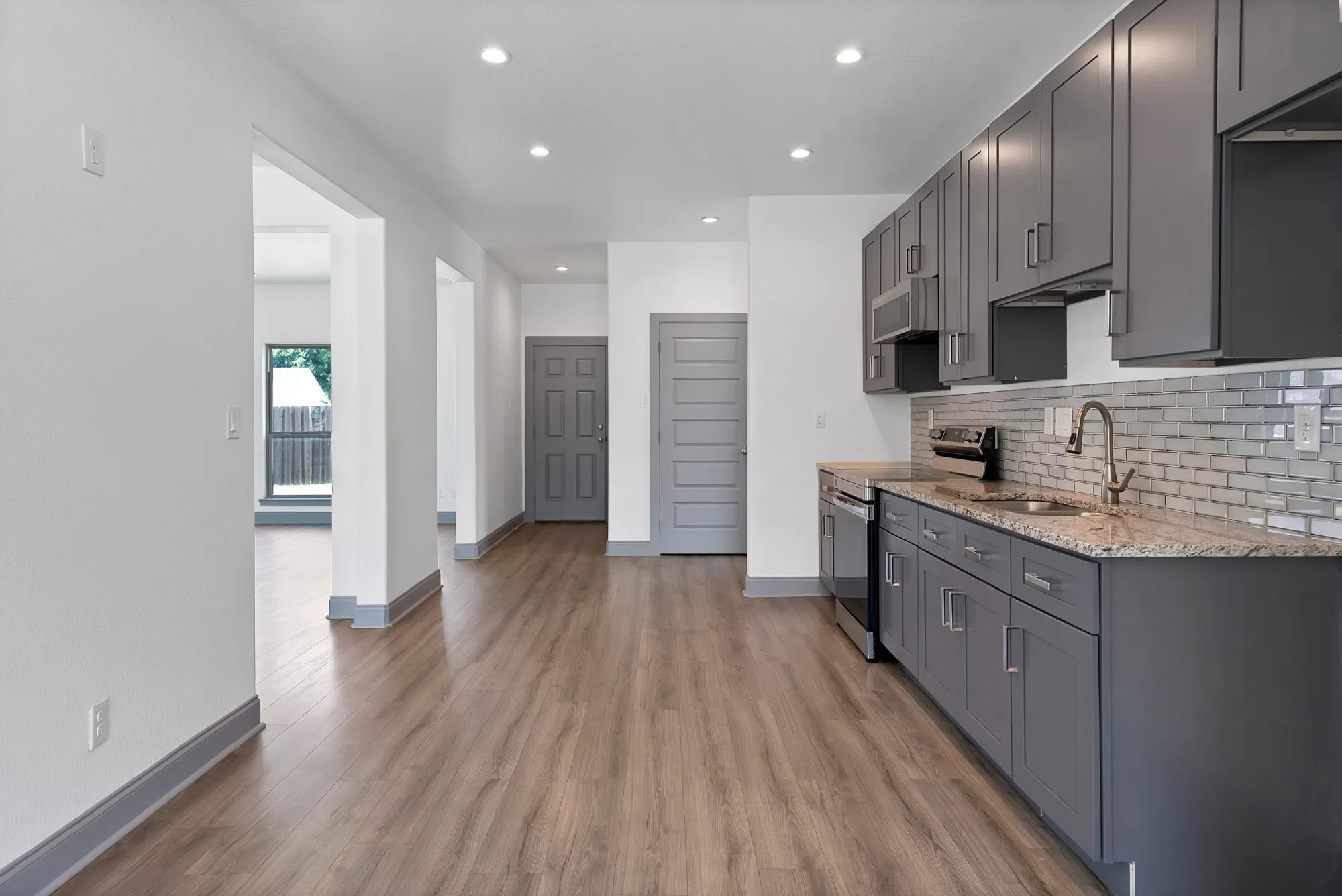 Modern kitchen featuring gray shaker-style cabinetry, a light-colored granite countertop, and a shimmering subway tile backsplash