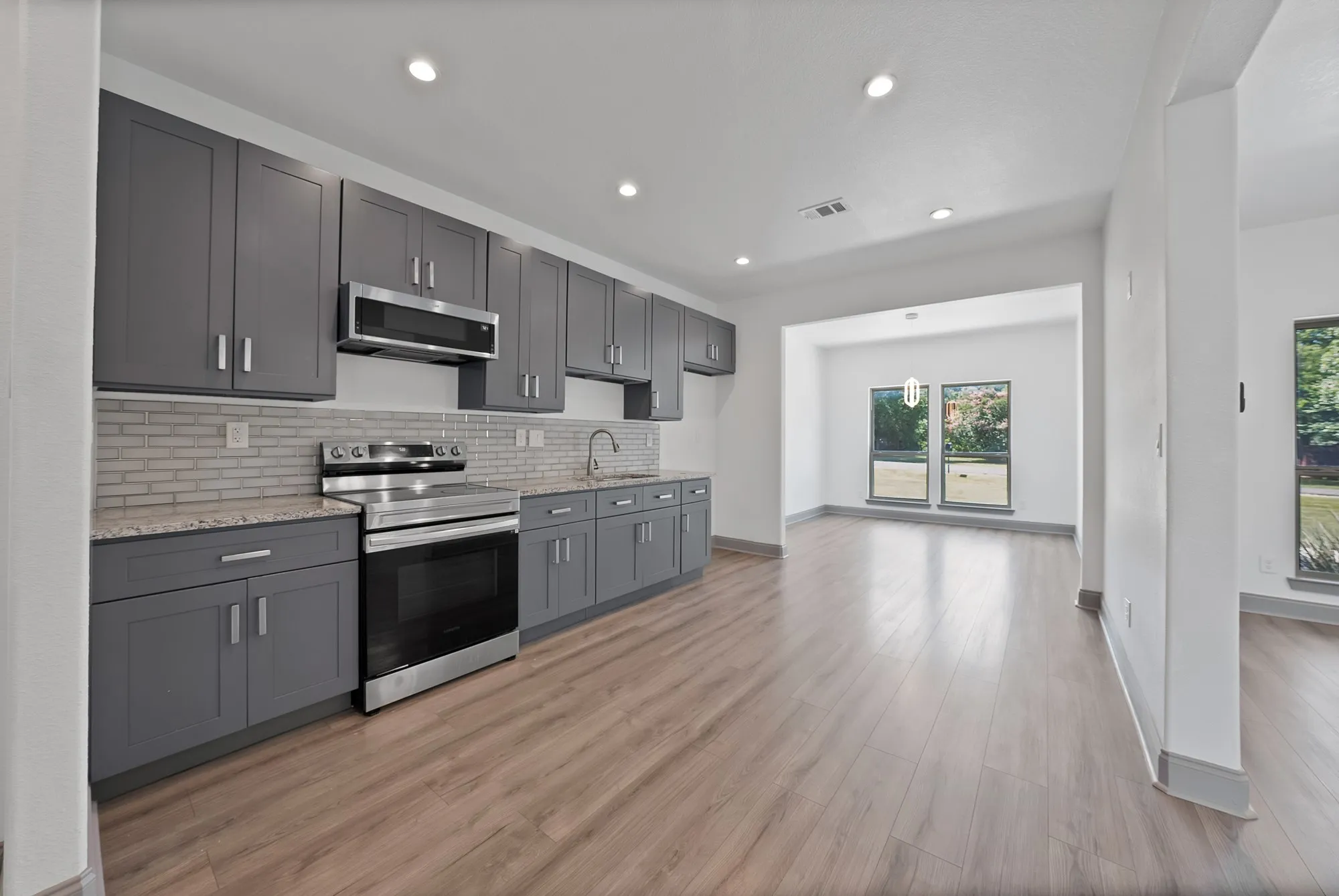 Open-concept kitchen featuring gray shaker-style cabinetry, stainless steel appliances, and granite countertops