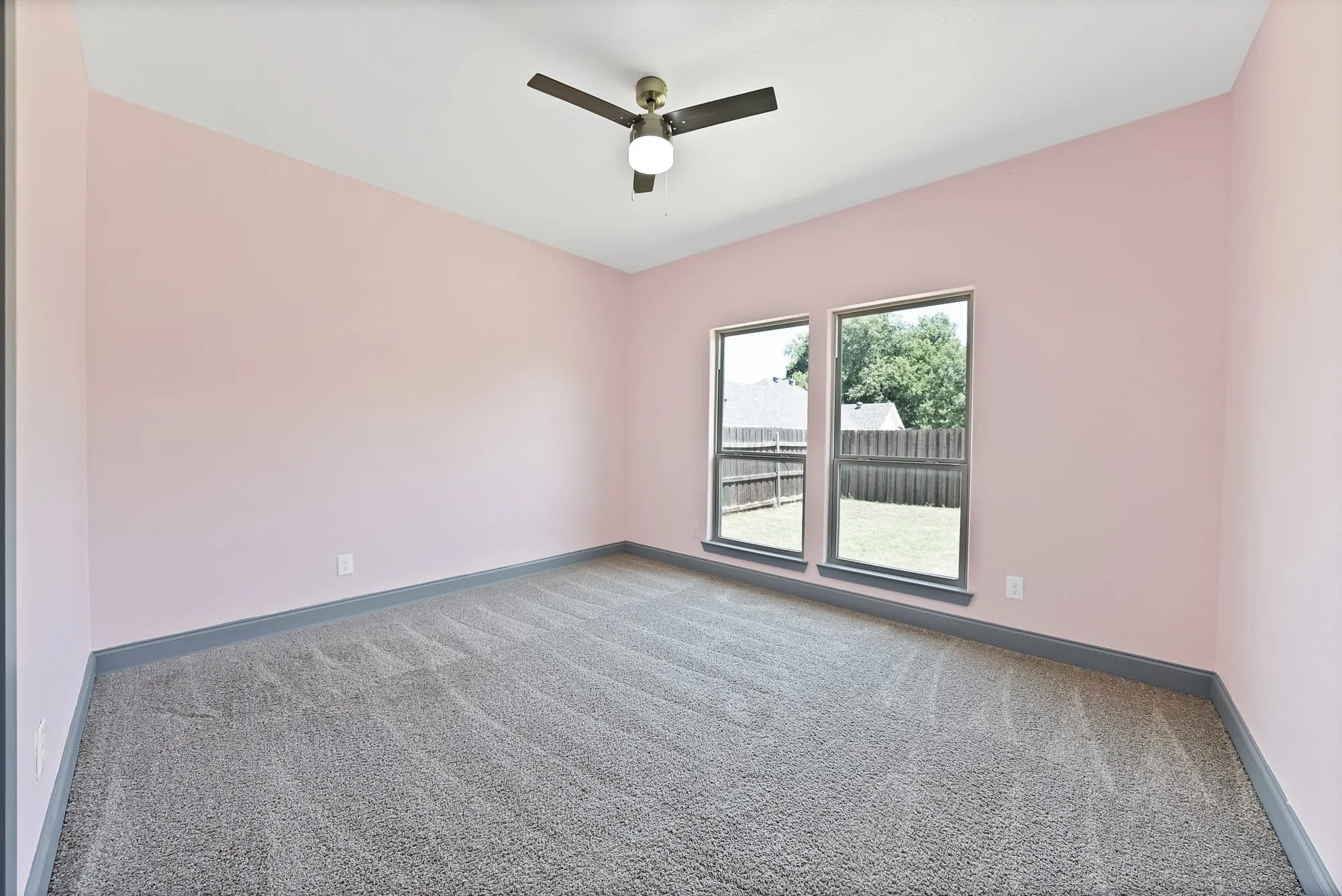 Spacious room featuring neutral carpet flooring, two large windows, a ceiling fan with integrated lighting, and a sloped ceiling