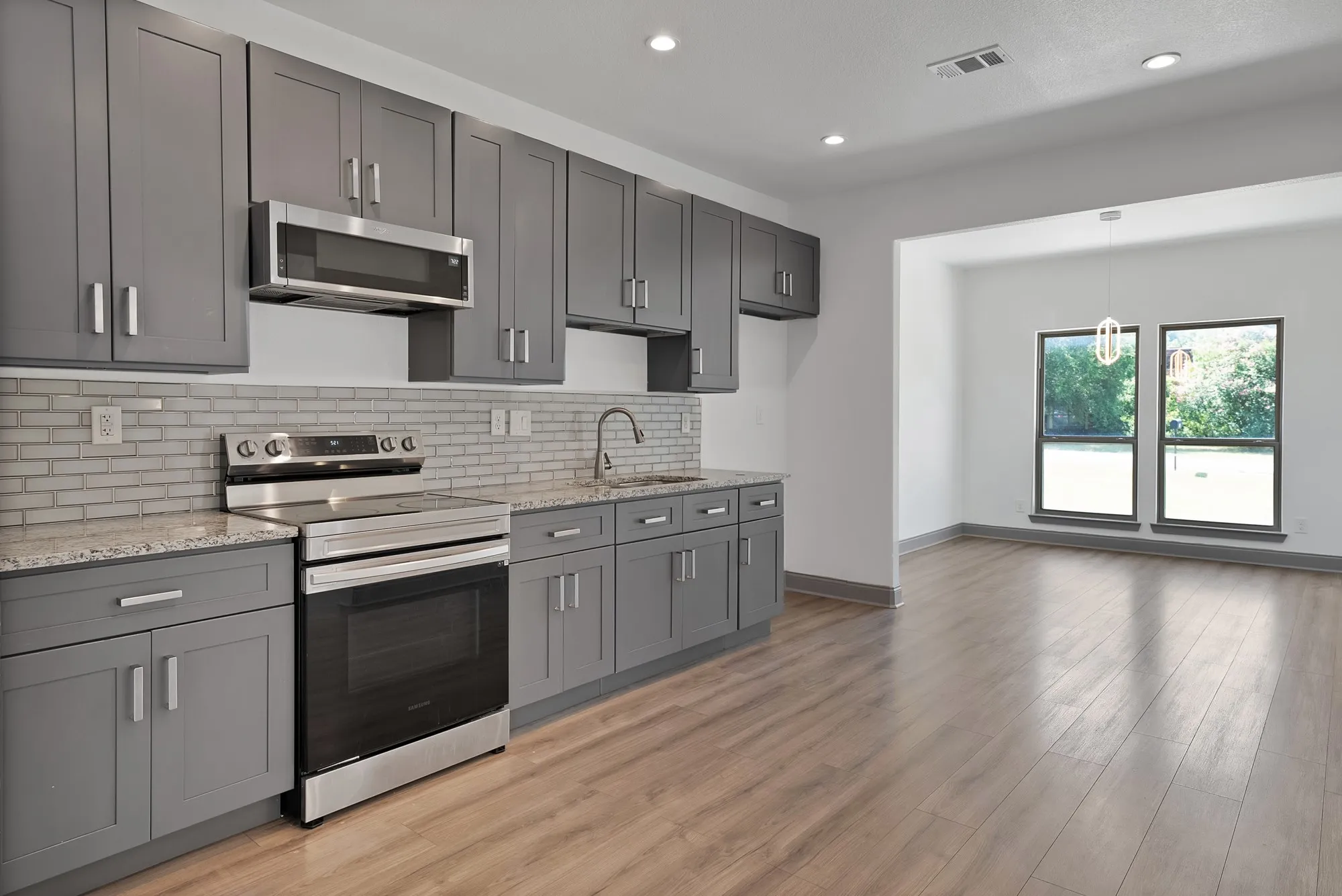 Kitchen featuring grey shaker-style cabinetry, granite countertops, subway tile backsplash, and stainless steel appliances
