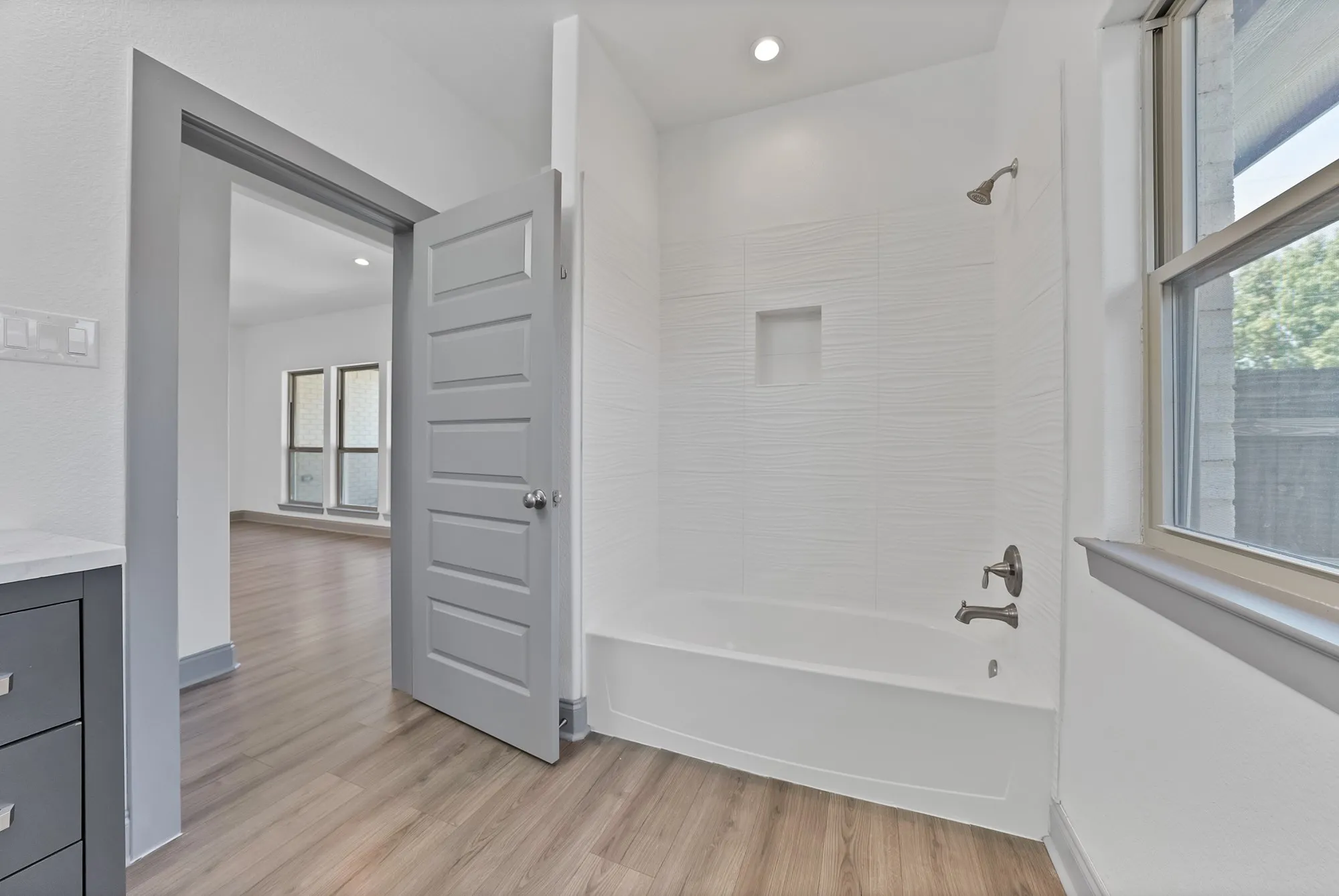 Bathroom featuring a white subway-tiled tub/shower combo with a built-in niche, modern brushed nickel fixtures, and a window for natural light