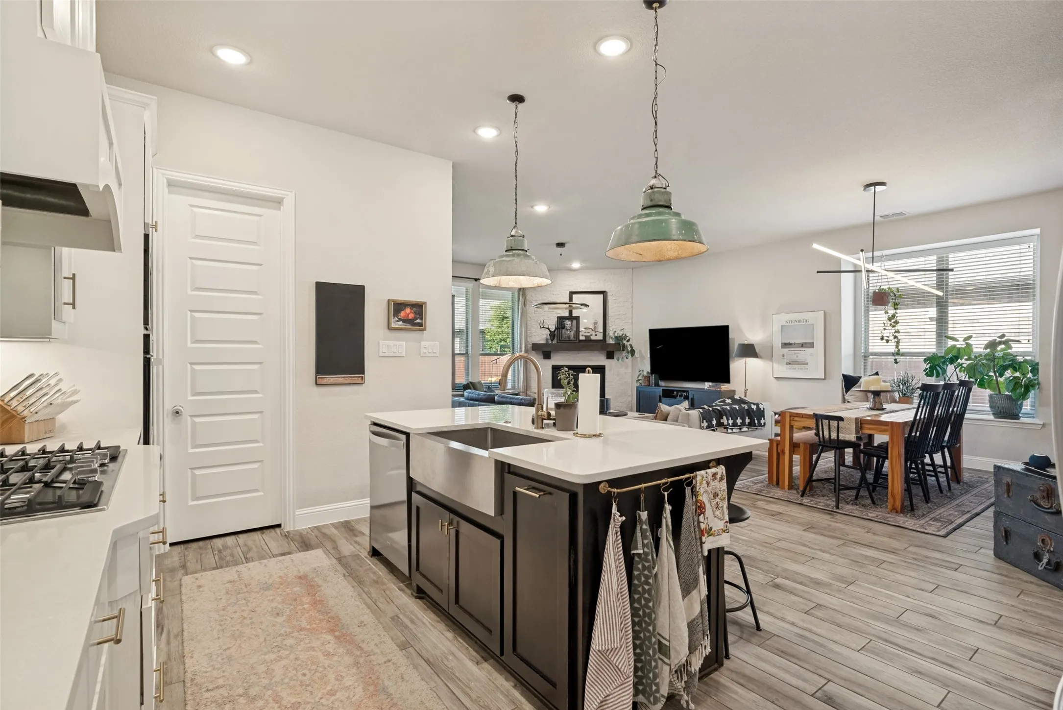 Kitchen island with a farmhouse sink and pendant lighting, featuring a gas range and wood-finish flooring