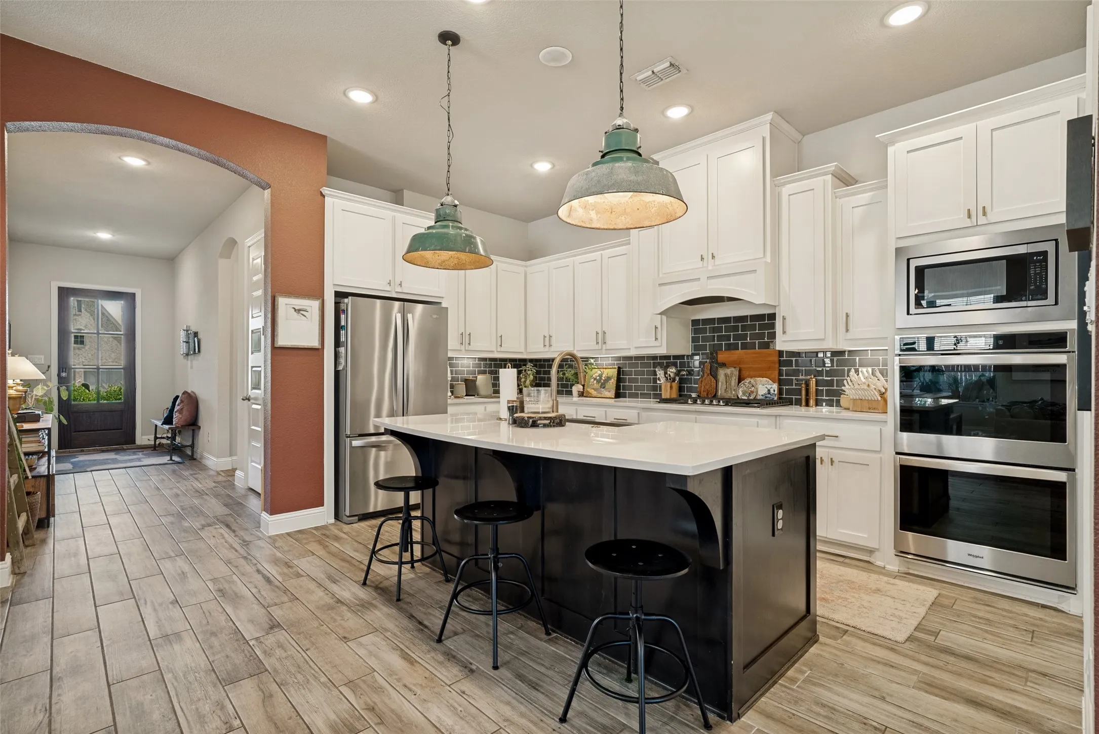 Kitchen featuring a large island with white countertop, white cabinetry, dark subway tile backsplash, stainless steel appliances, and wood-finish flooring