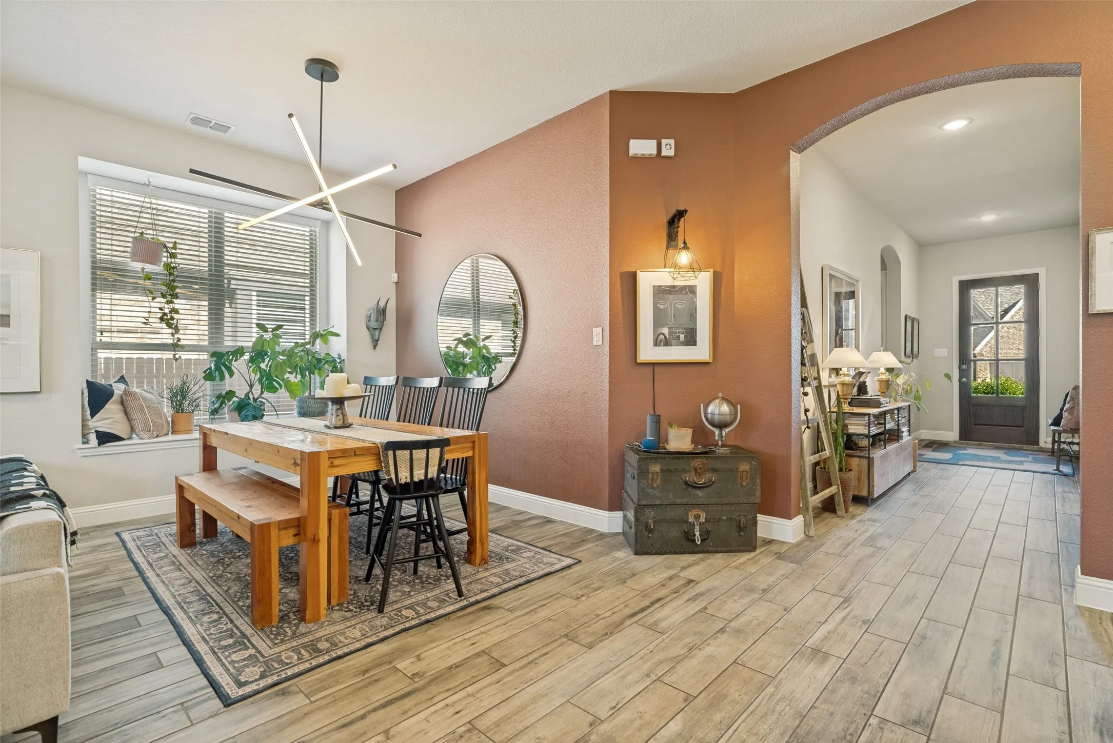 Open-concept dining area featuring wood-finish flooring, a contemporary linear chandelier, and a built-in window seat