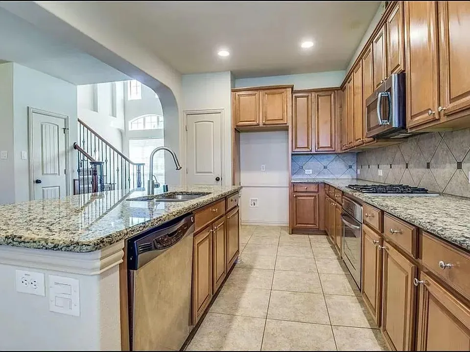 Kitchen featuring an island with granite countertops, stainless steel sink with gooseneck faucet, light wood cabinetry, and a gas cooktop