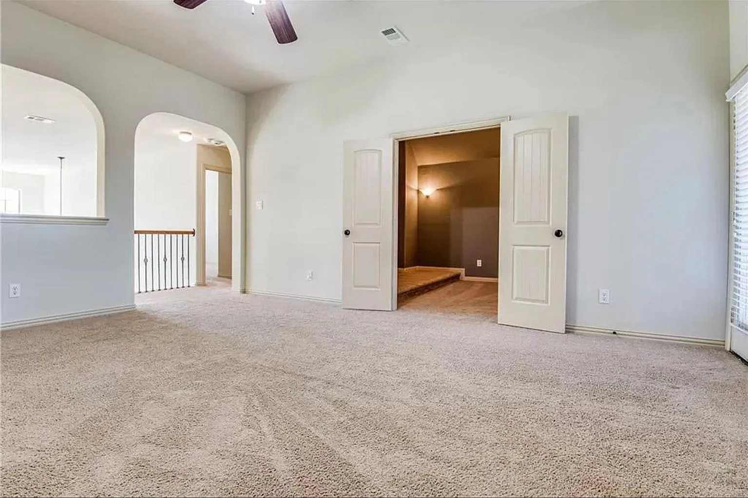 Carpeted interior space featuring light-toned walls, a ceiling fan, and arched openings