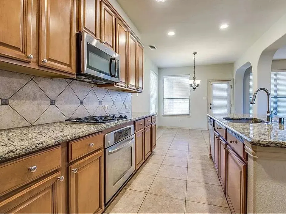 Kitchen featuring wood cabinetry, granite countertops, tile flooring, and stainless steel appliances including a built-in oven and microwave