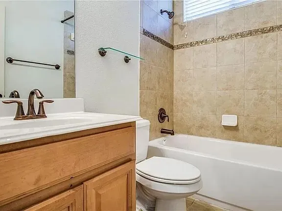 Bathroom featuring a white vanity with a bronze-finish faucet, a toilet, and a tiled shower-tub combination