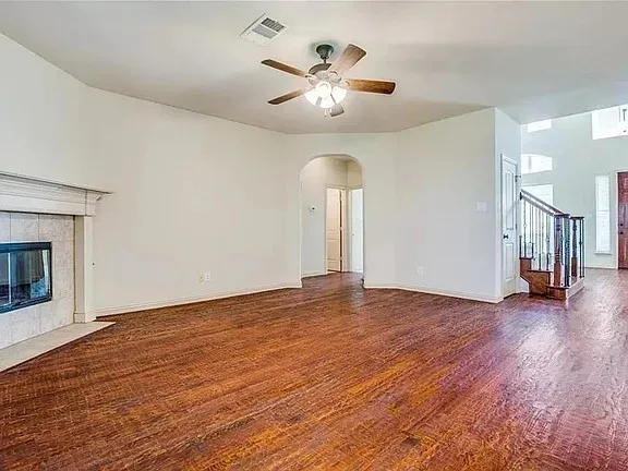 Spacious living area featuring wood-finish flooring, a tiled fireplace with a white mantel, and an arched doorway