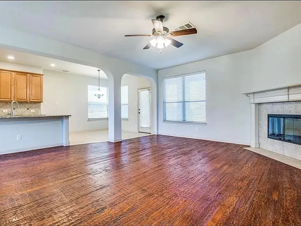 Spacious living area featuring wood-finish flooring, a ceiling fan with integrated lighting, and a fireplace with a mantel and tile surround