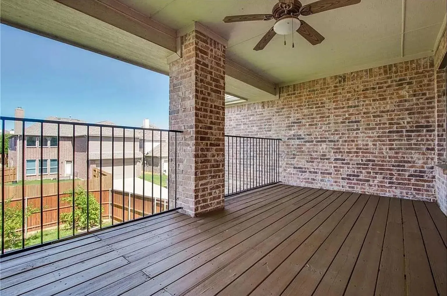 Covered outdoor balcony featuring wood-finish flooring, a brick exterior wall, black metal railing, and a ceiling fan