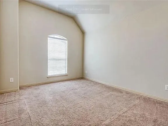 Vaulted ceiling room featuring a single arched window with blinds, neutral wall paint, light brown carpet, and matching baseboards