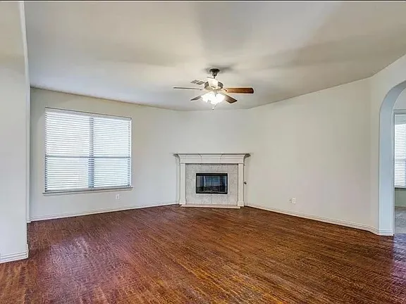 Spacious living area featuring rich wood-finish flooring, a contemporary fireplace with a decorative mantel, and a ceiling fan with light fixture