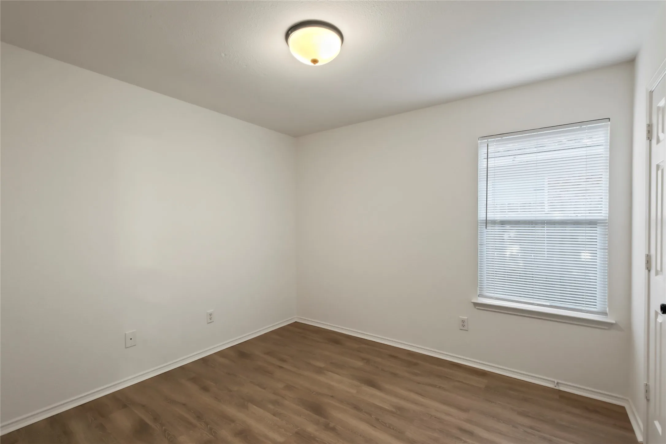 Room with wood-finish flooring, light-colored walls, and a single window with blinds