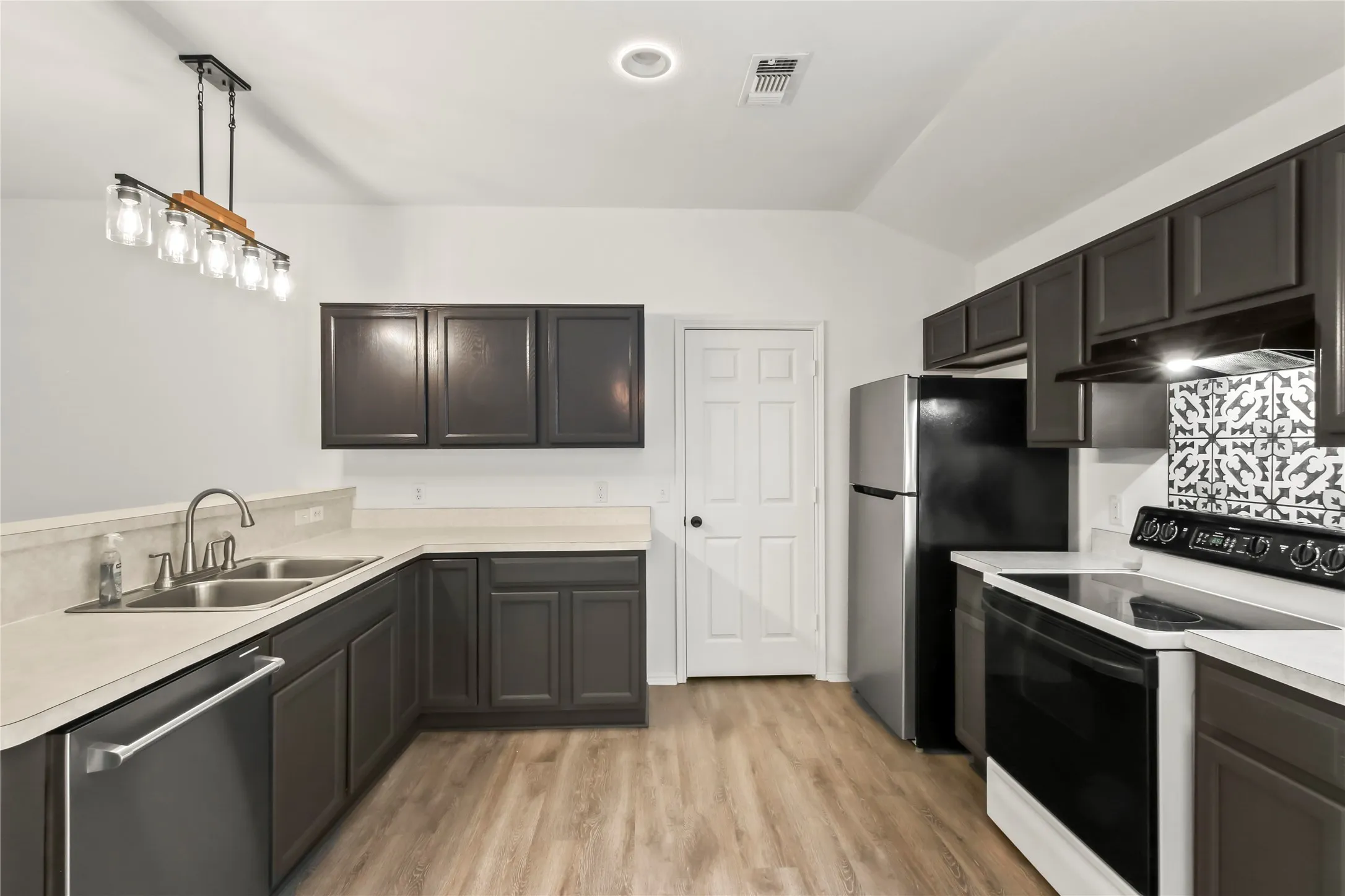 Modern kitchen featuring dark cabinetry, light countertops, stainless steel sink, wood-finish flooring, and a decorative tile backsplash