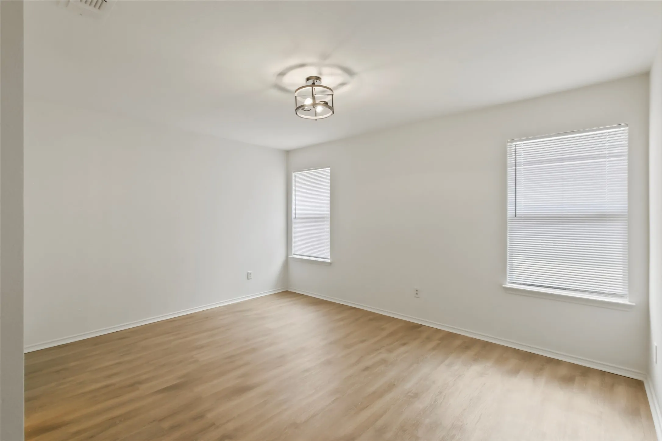 Spacious room featuring wood-finish flooring, white baseboards, and neutral wall tones