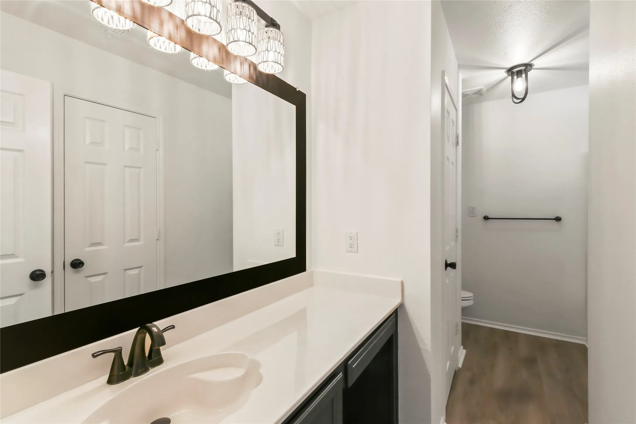 Contemporary vanity featuring a white countertop with integrated sink, dark bronze faucet, and a rectangular mirror