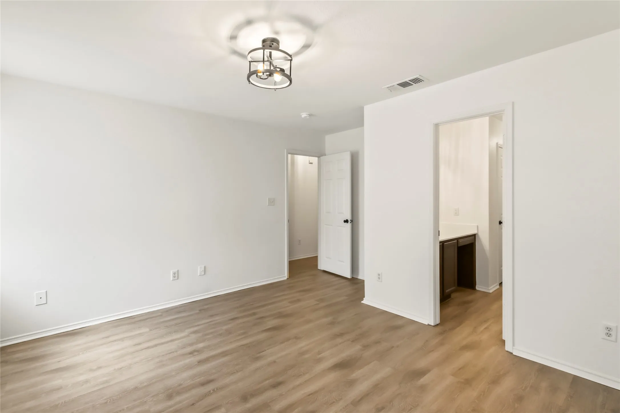 Spacious room featuring wood-finish flooring, white walls, and a contemporary semi-flush mount light fixture