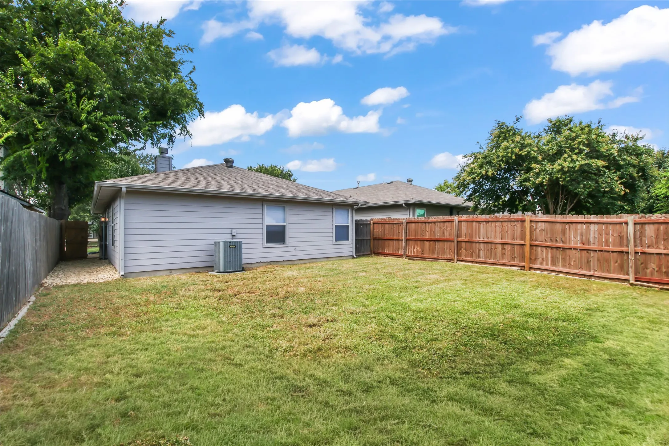 Expansive backyard featuring a manicured lawn, full privacy fencing, and mature trees