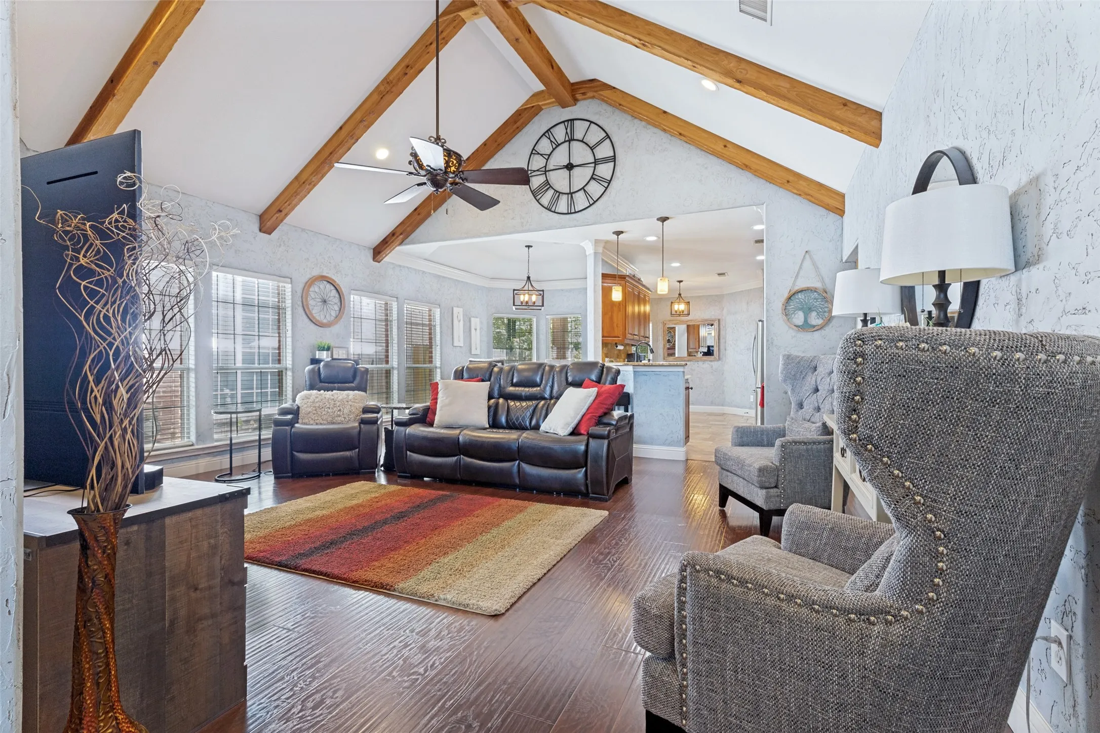 Living area featuring vaulted ceilings with exposed wood beams, dark wood-finish flooring, and multiple windows